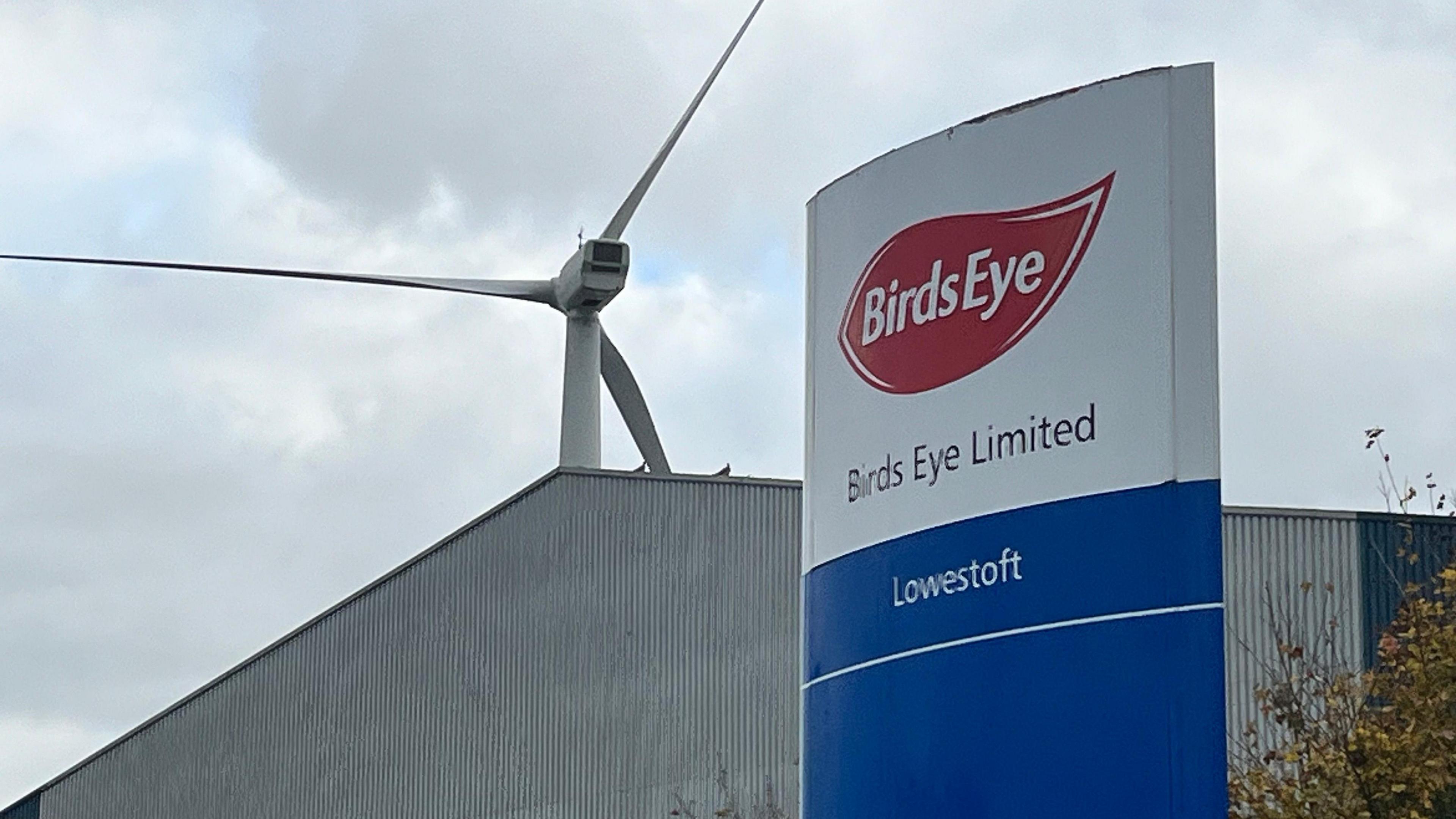 An onshore wind turbine can be seen over a blue and white sign reading "Birds Eye Limited Lowestoft".