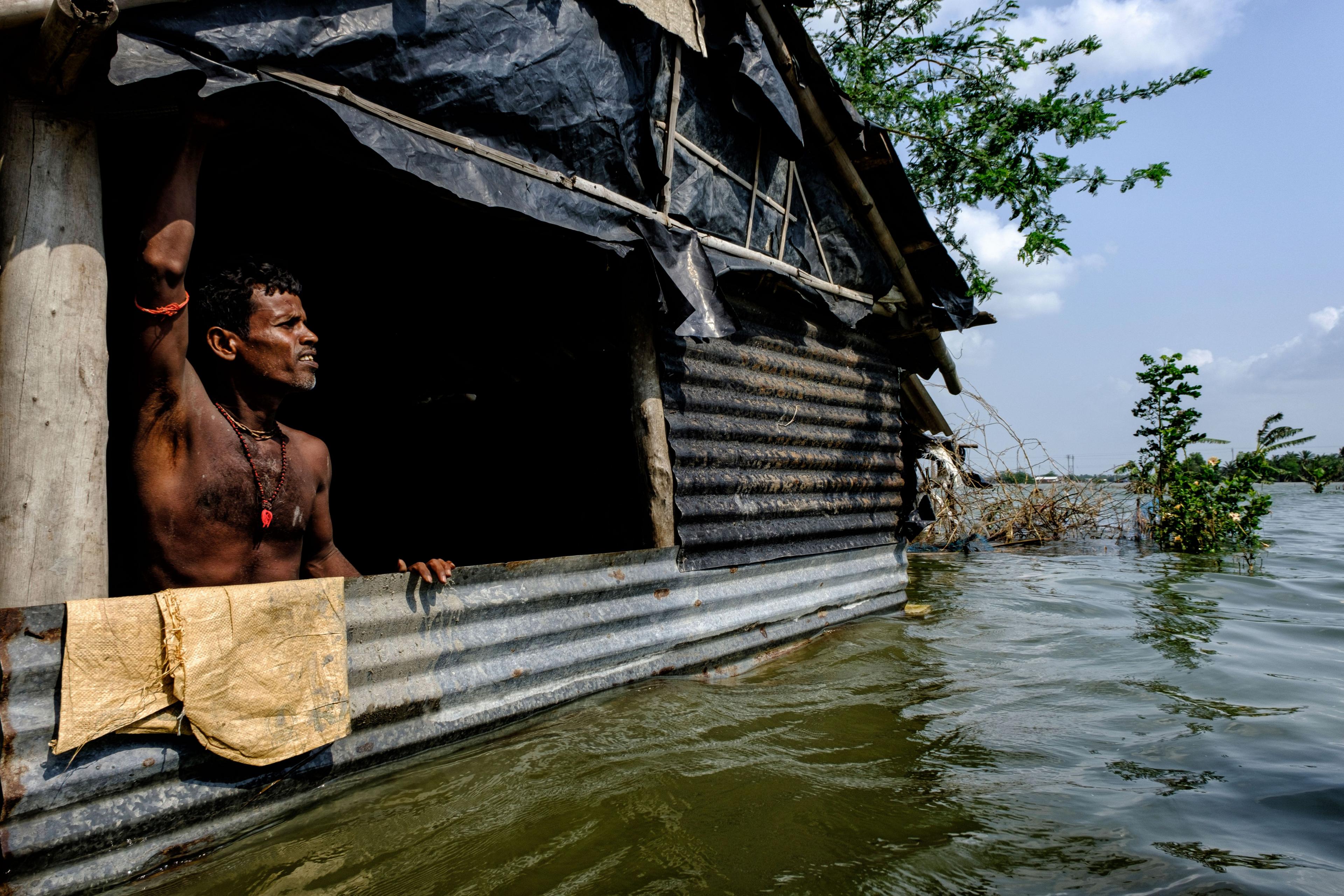 A villager standing inside his half-submerged home during a flood in the Sundarbans, West Bengal, India