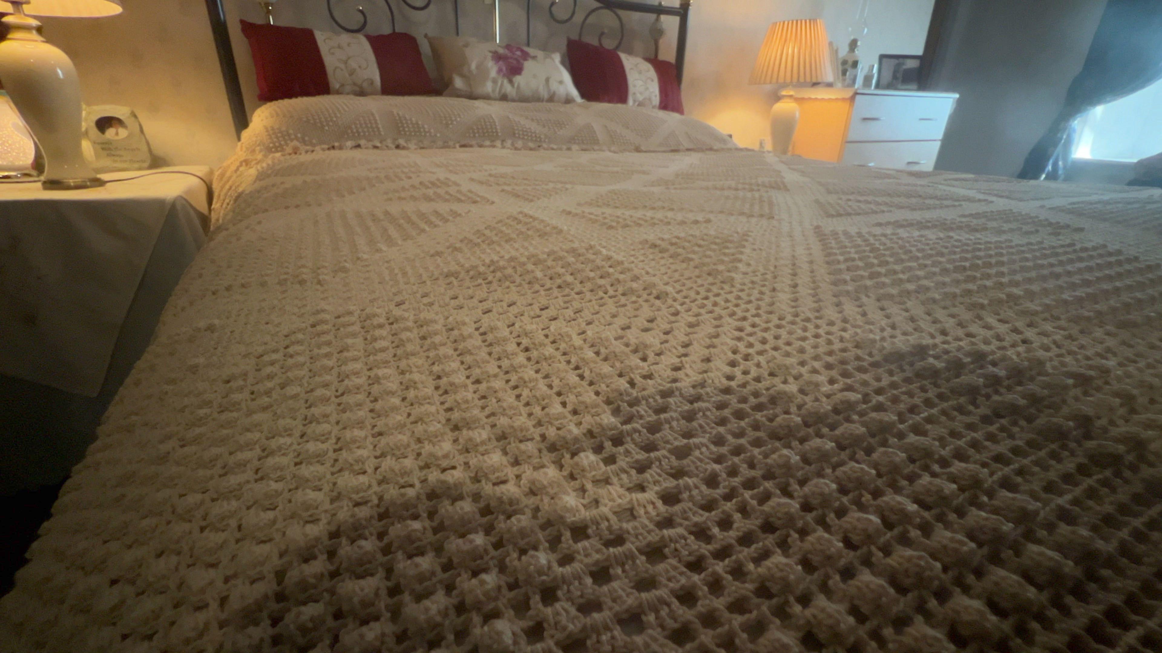 A closer shot of the crocheted bedspread which lies neatly on top of a double bed.