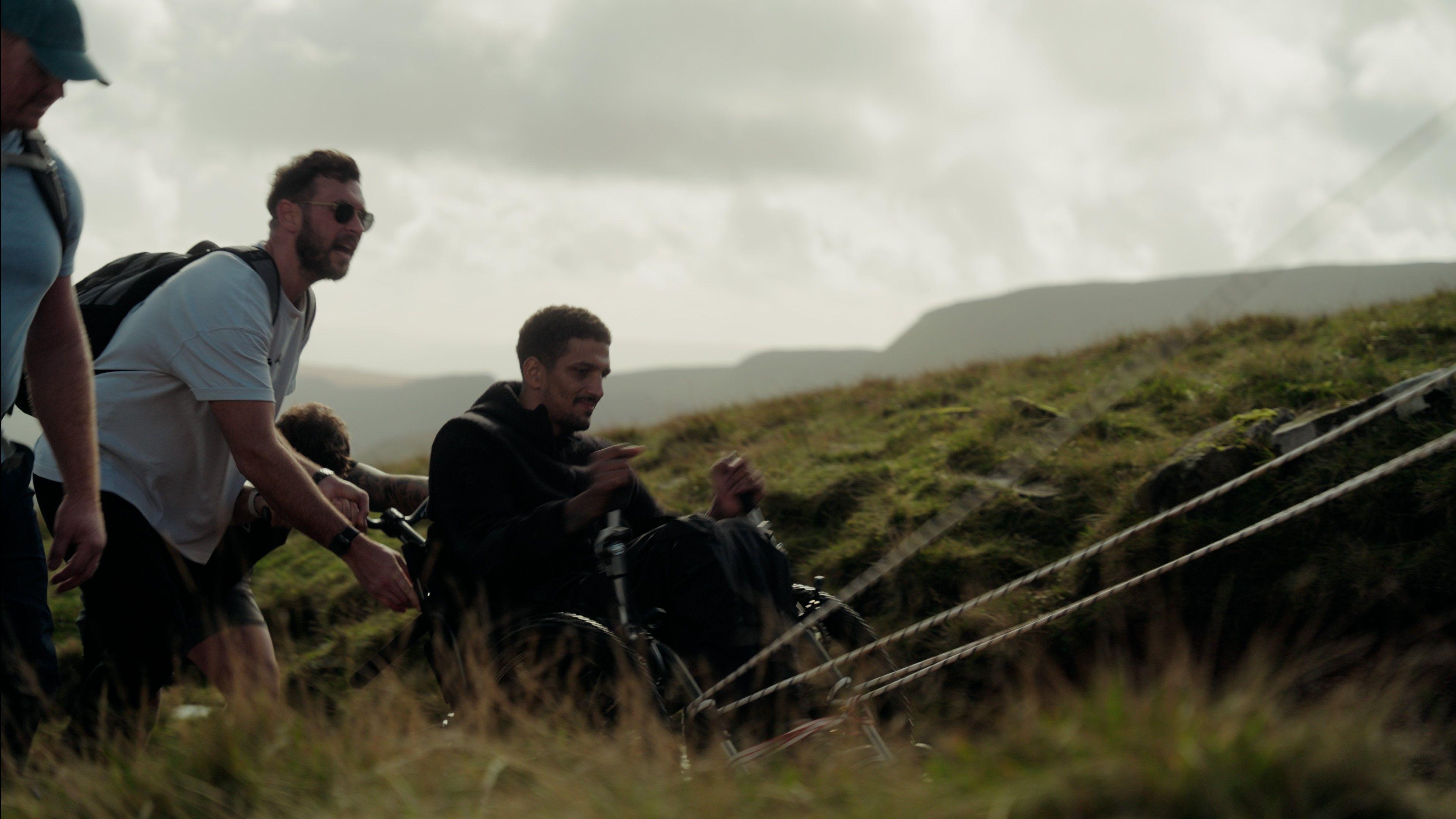 Liam O'Keeffe pushing himself up Pen Y Fan in his specially-adapted wheelchair. Three men can be seen behind him helping to push him forward.