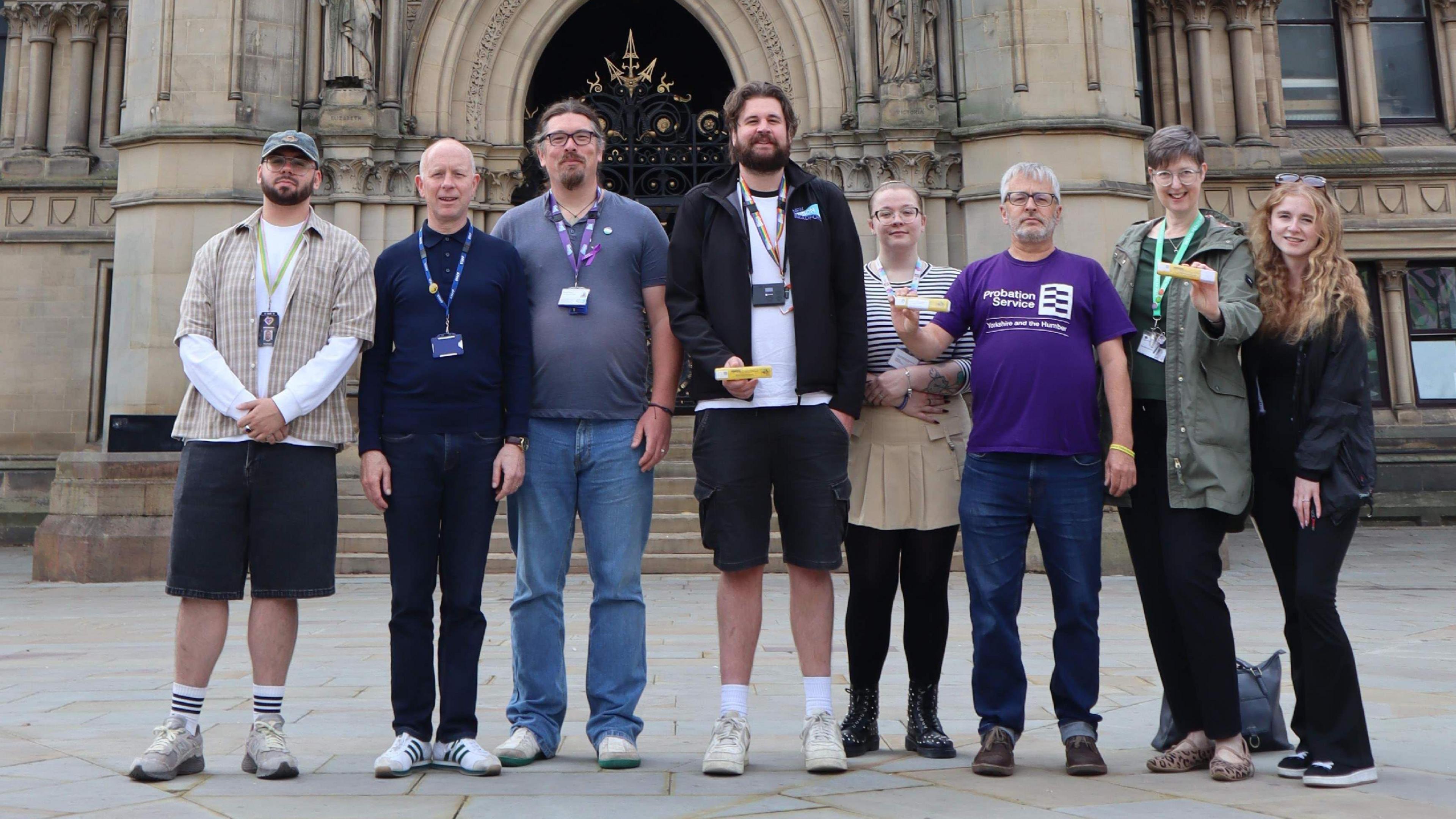 A line up of men and women with some holding a small yellow box which contains the Naloxone syringe