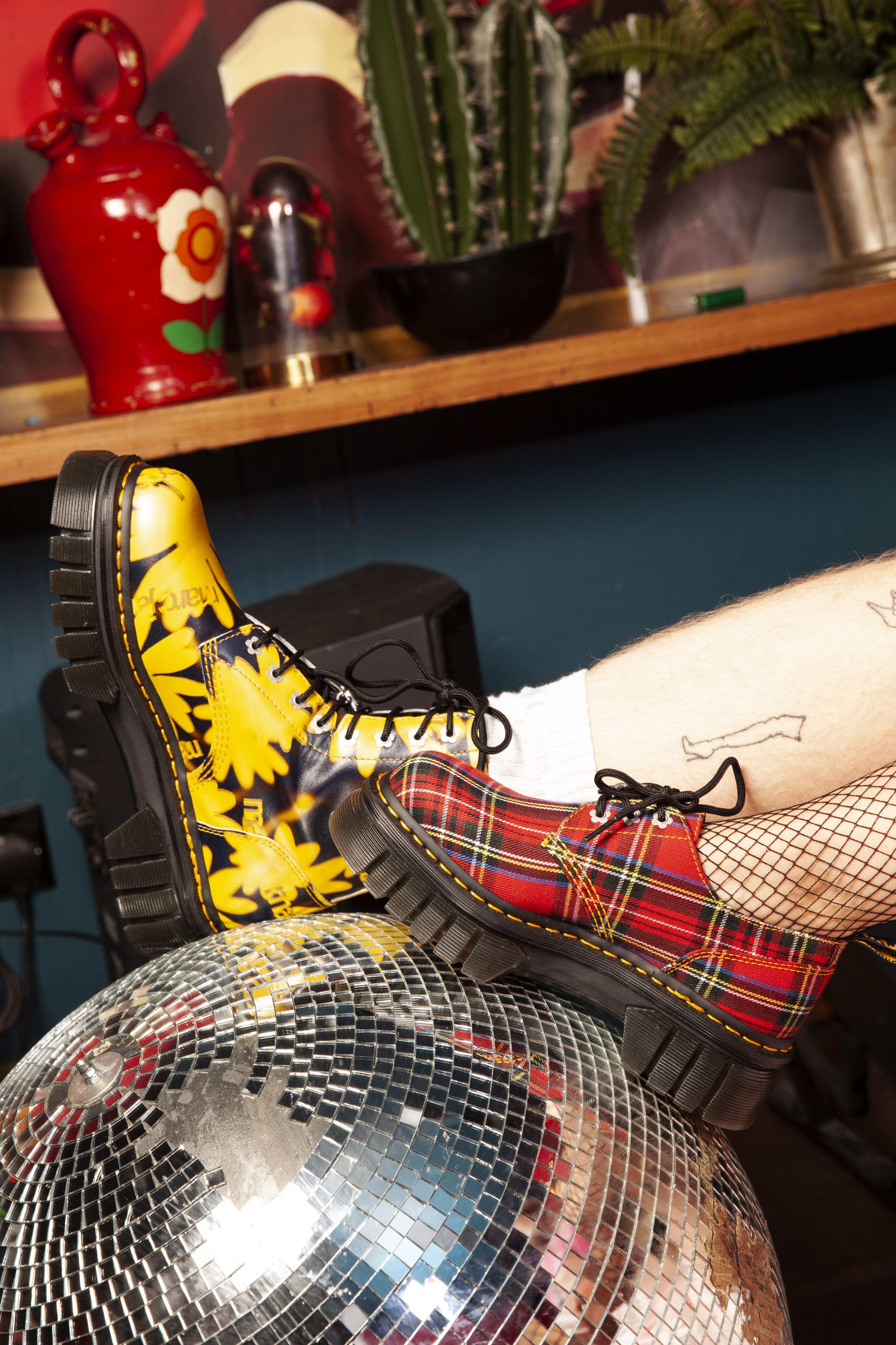 A red chequered Dr Marten boot and a yellow and clack floral Dr Marten boot on a glitter ball