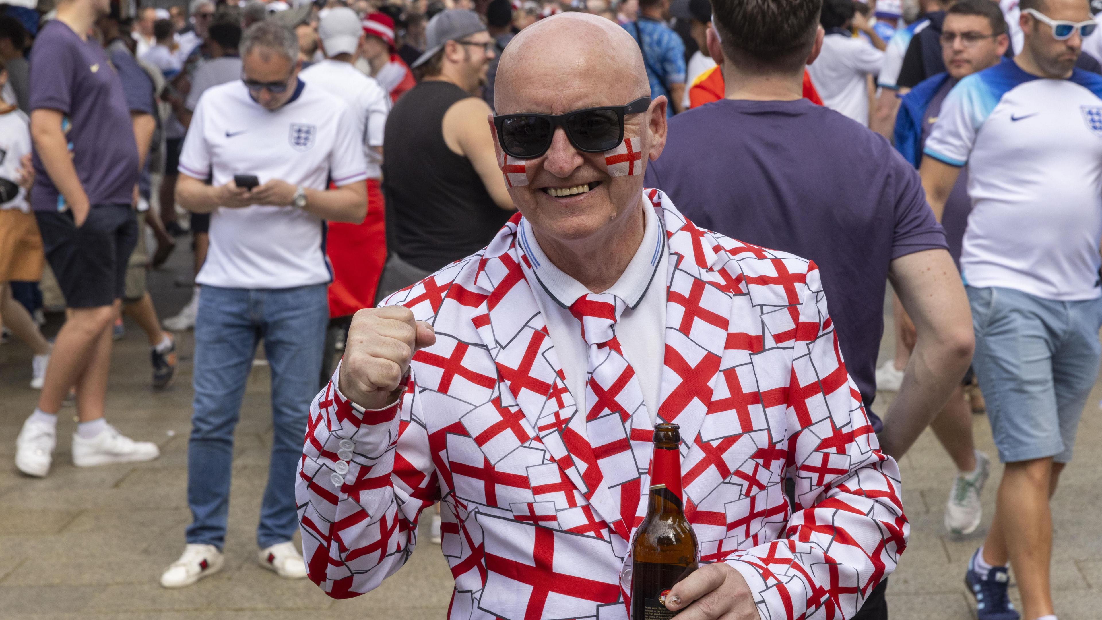 A man wears a suit covered in the England flag and has on a pair of black sunglasses