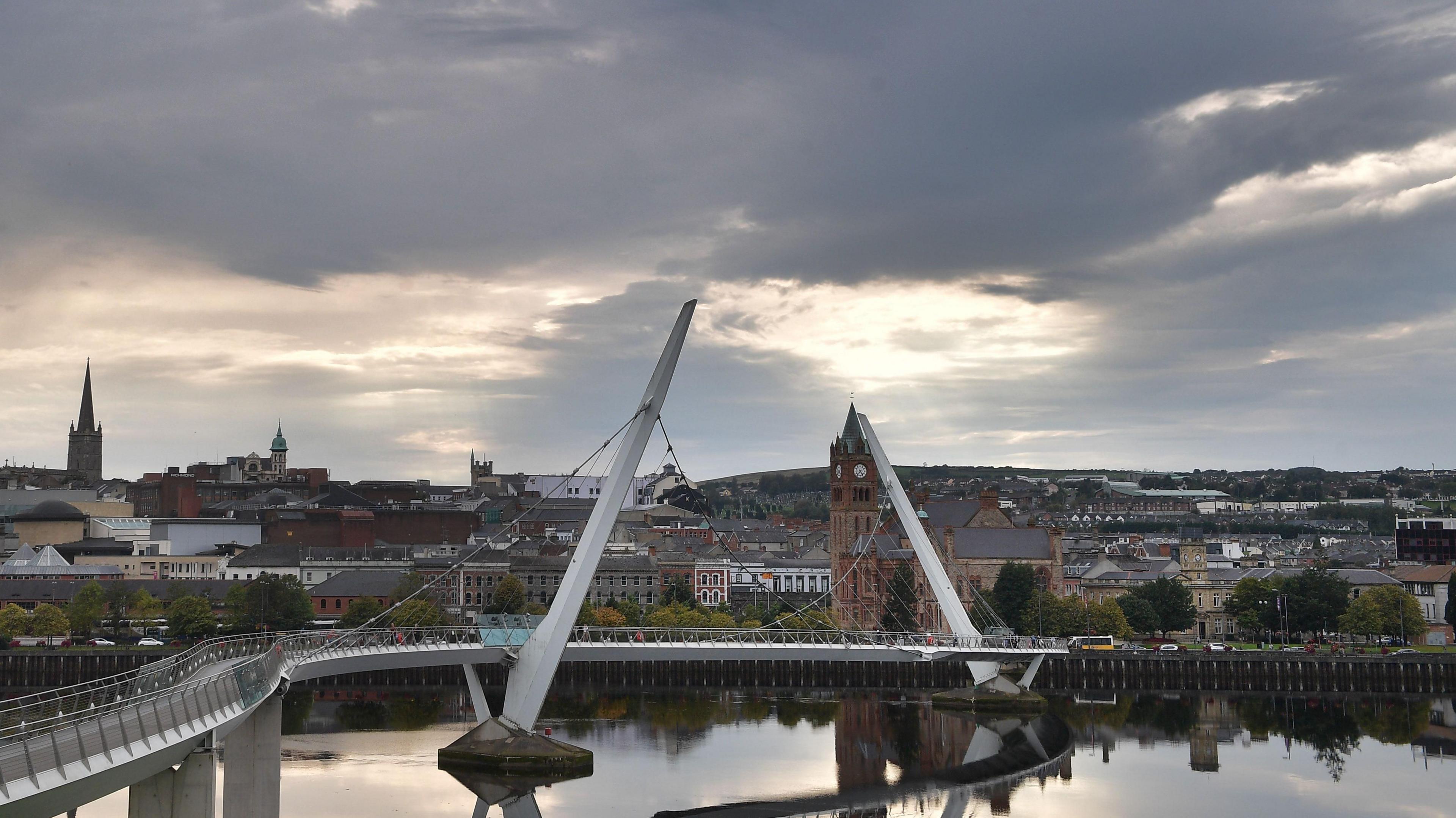 Shows Derry's peace bridge beneath grey skies with the Guildhall, St Columb's Cathedral and other buildings in the background.