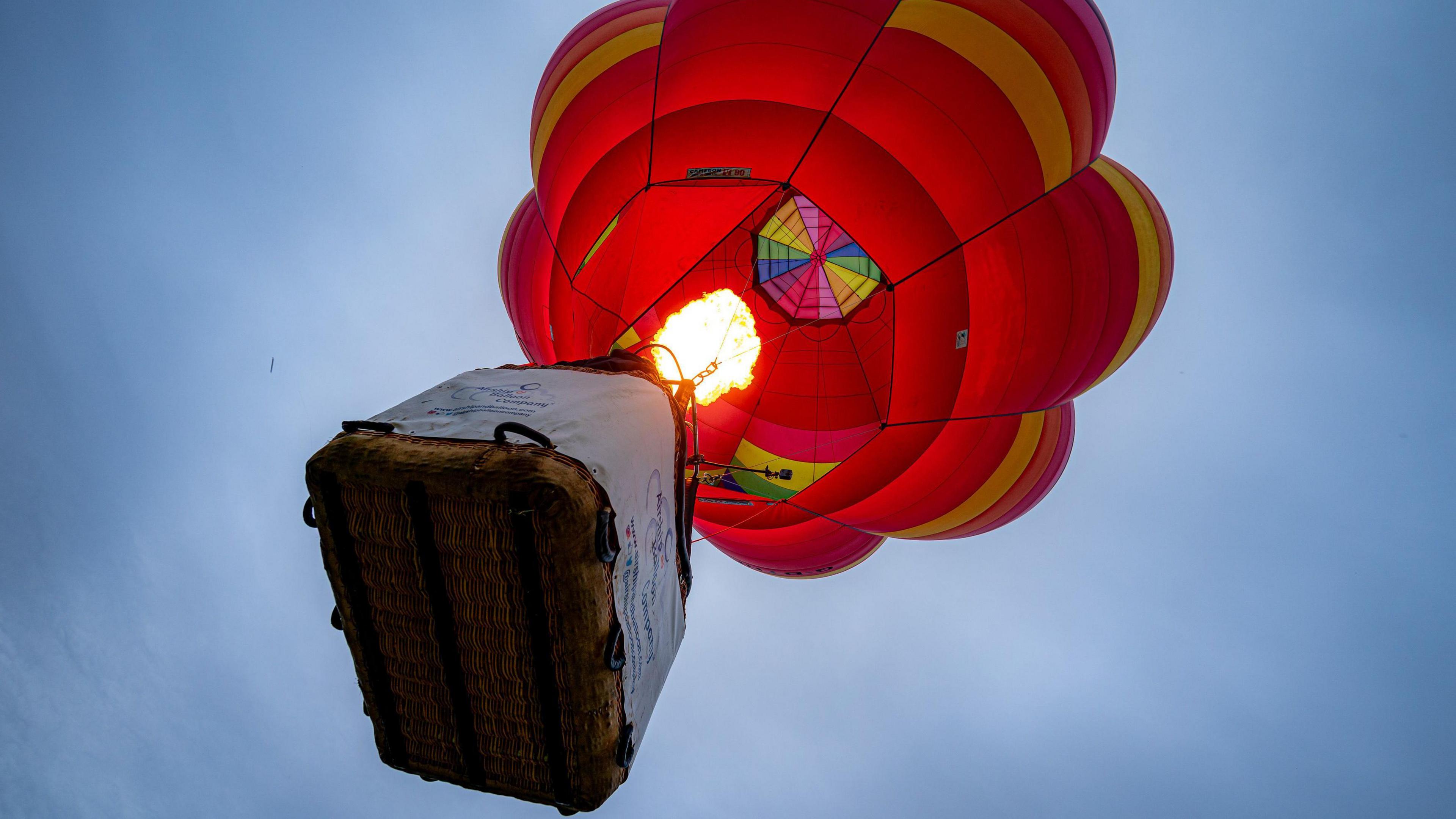 A colourful hot air balloon is seen from below at the Bristol Balloon Fiesta. The flame from its burners is visible