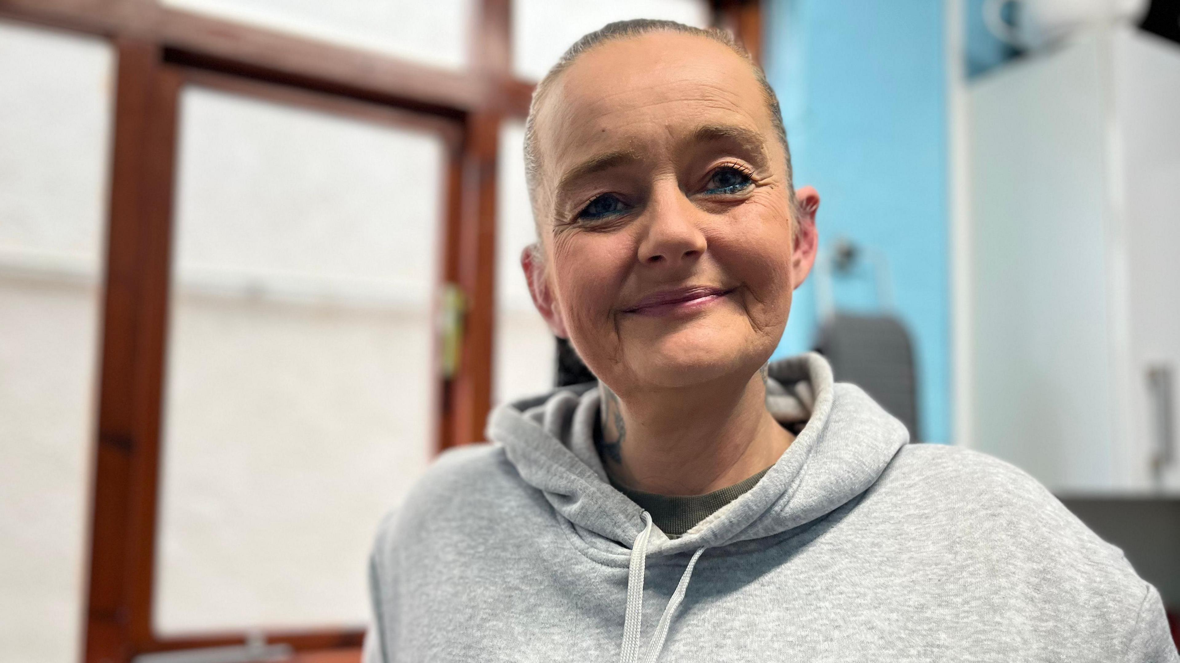 Jo Evans is looking directly at the camera and smiling. She has her hair pulled back into a ponytail and is wearing a grey hooded sweatshirt.