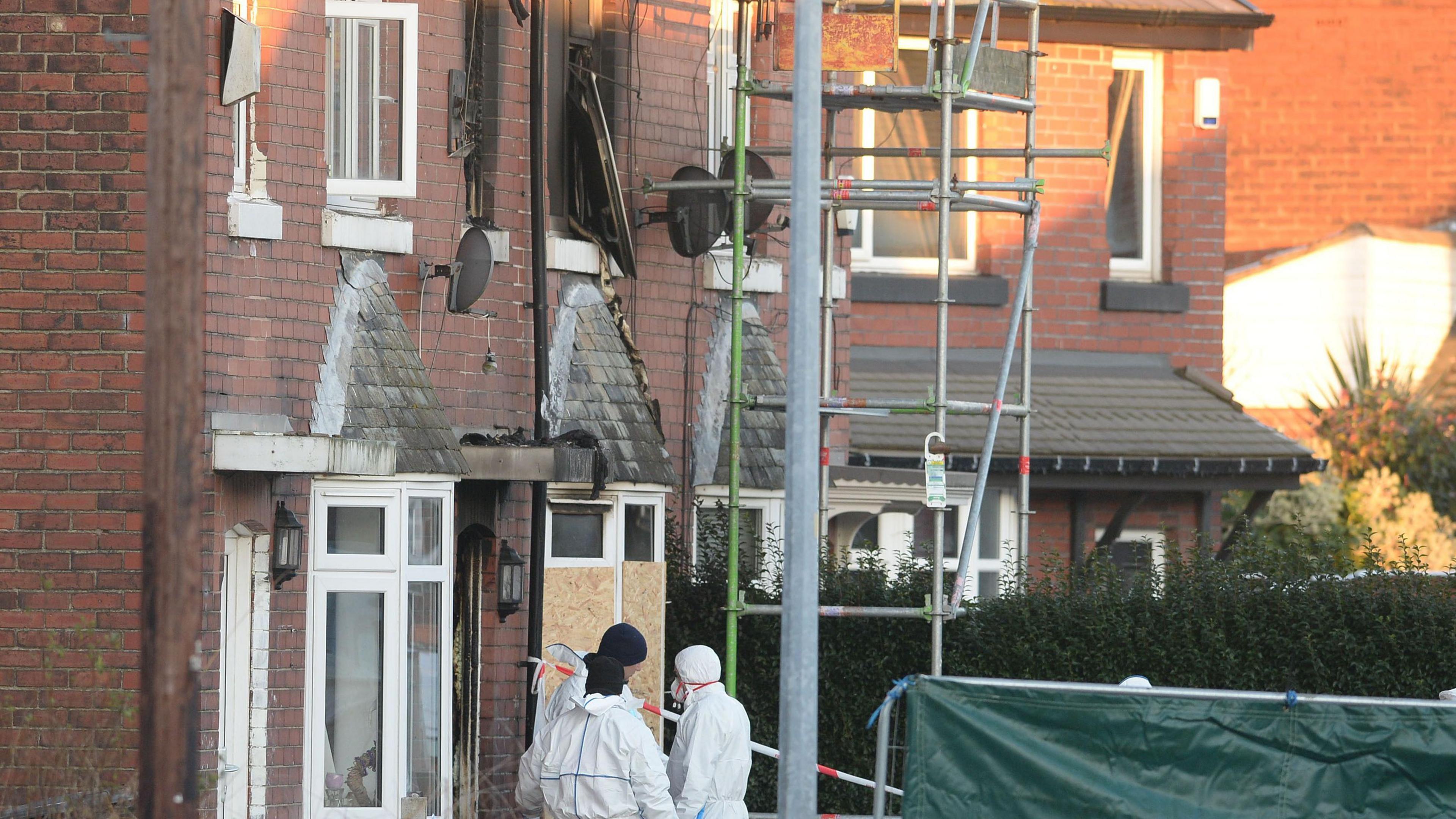 Forensic officers at the scene of a house fire in Walkden, Greater Manchester which shows upstairs windows blown out, smoke damage and windows boarded up.