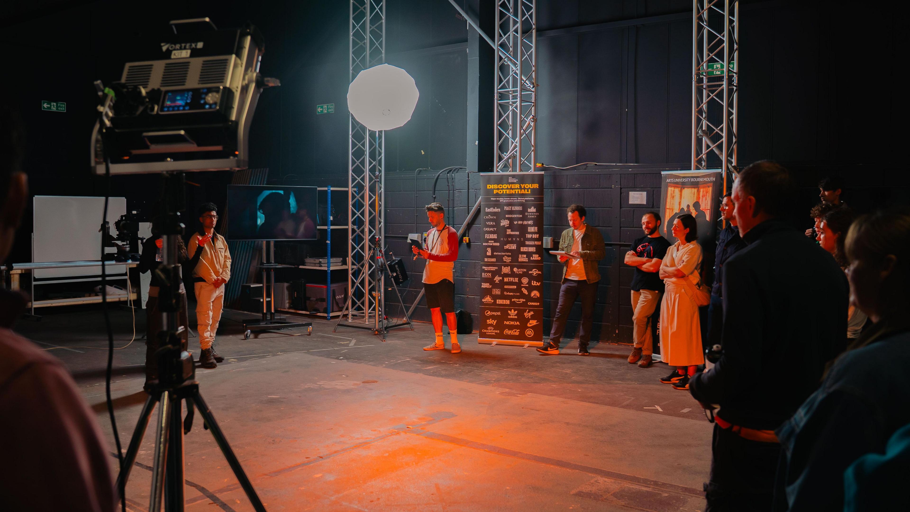 Students are on an interior sound stage. There are lights, cameras, and a large screen.