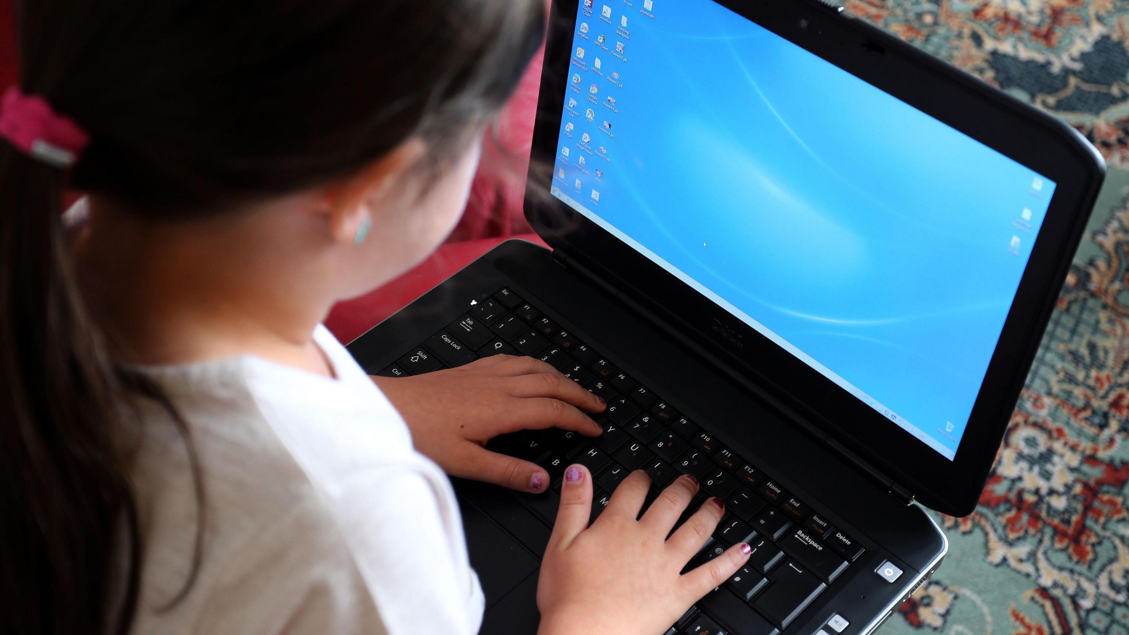 A small girl with a pony tail hairstyle and pink nail varnish uses a laptop.