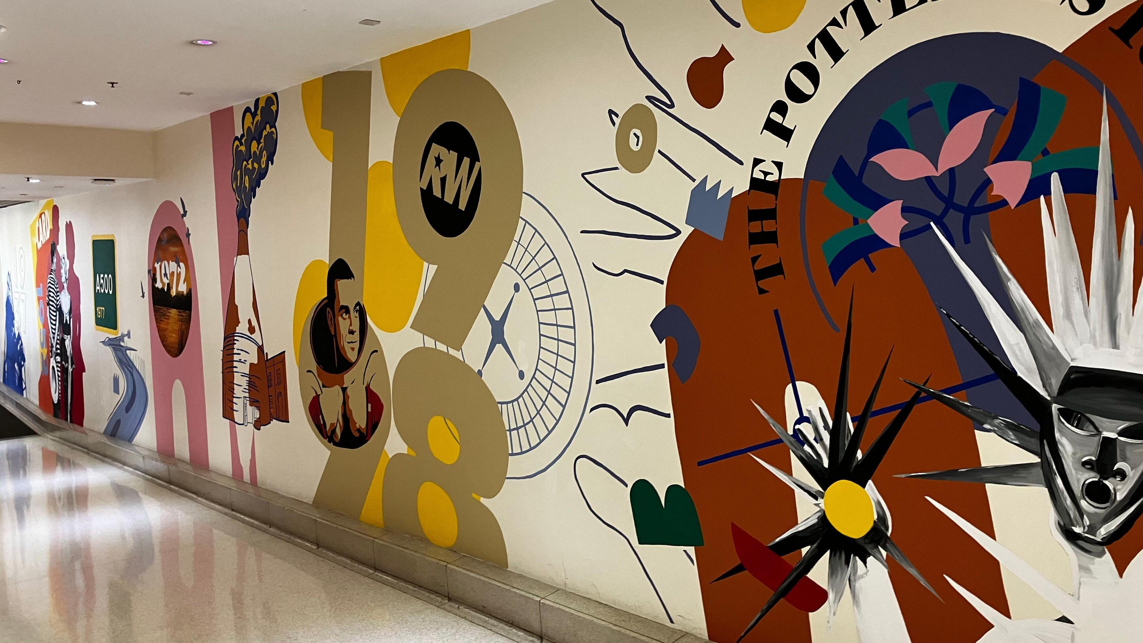 A wall that has multiple murals painted featuring different prominent years in the History of Stoke-on-Trent. There is one specifically of Robbie Williams where his face appear in the numbers of 1998 referring to the year he got his first number one single.