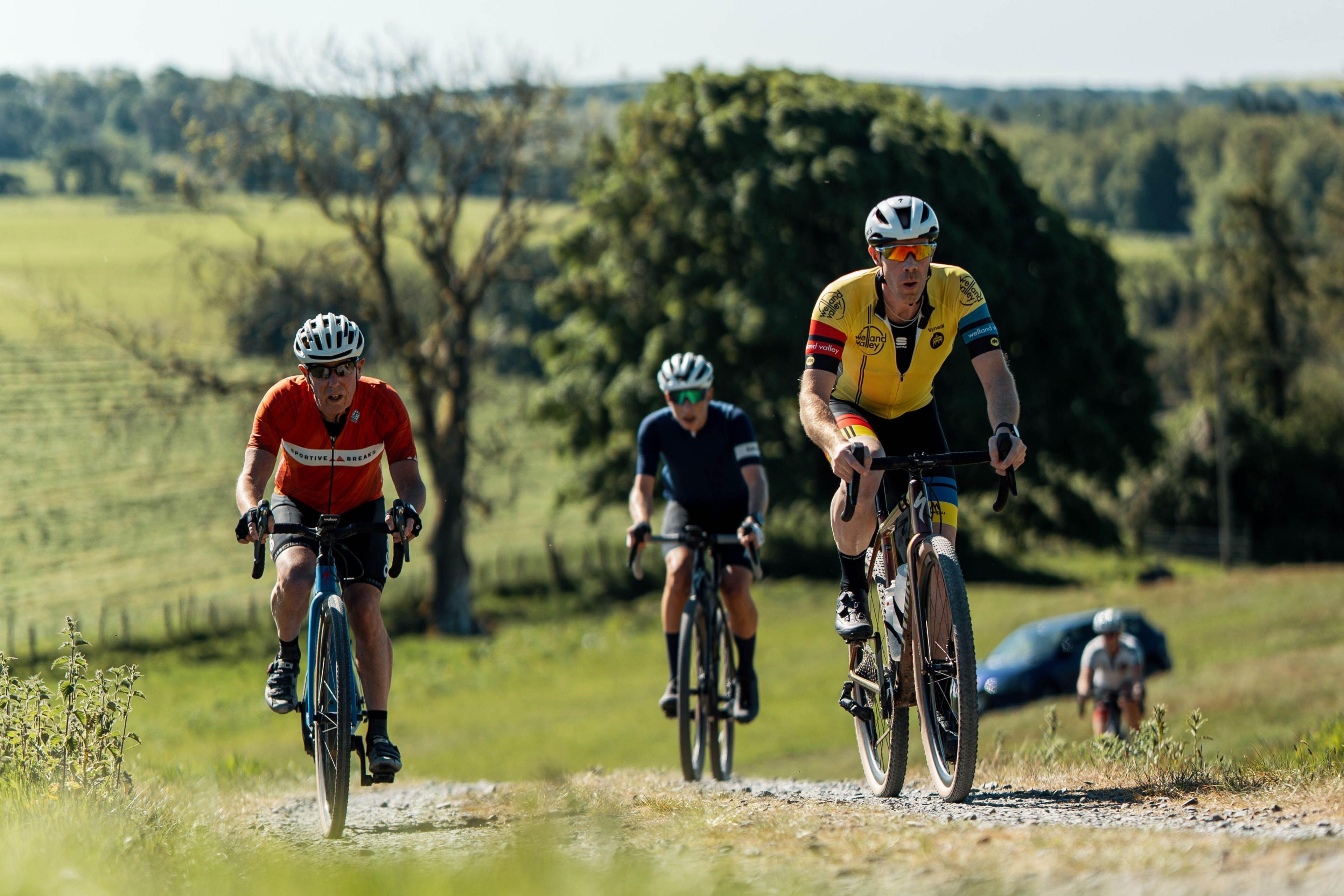 Four cyclings head up a hill on a gravel path through lush, green countryside