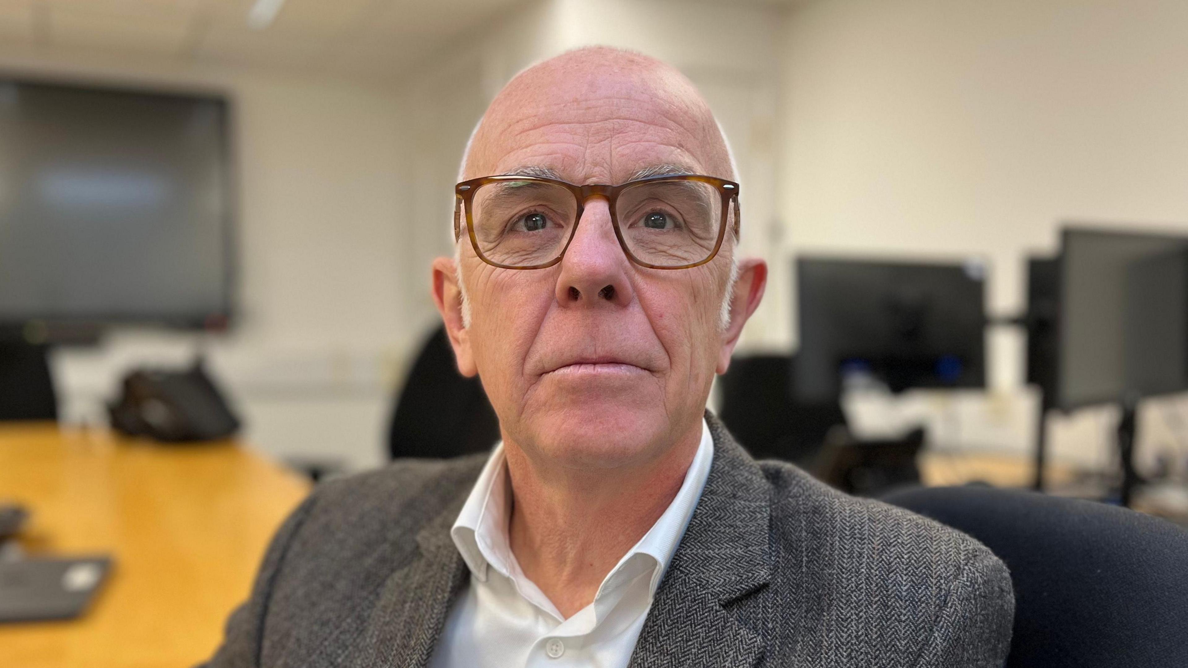 Dr Steve Evans - A bald man, with white wispy hair on the side of his head. He is wearing brown spectacles, a grey jacket and a white shirt.