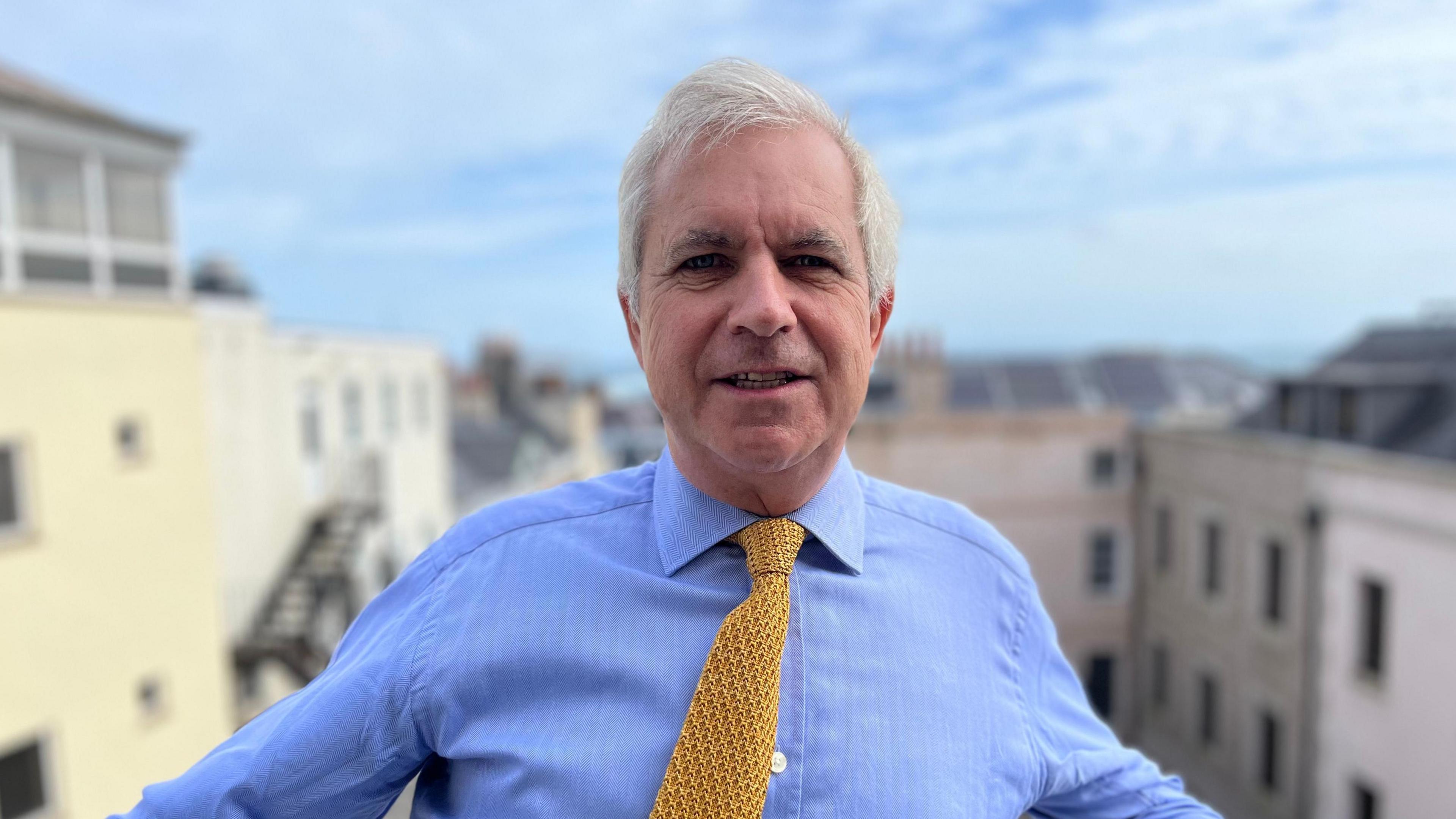 A man with a blue shirt and yellow tie looking towards the camera.