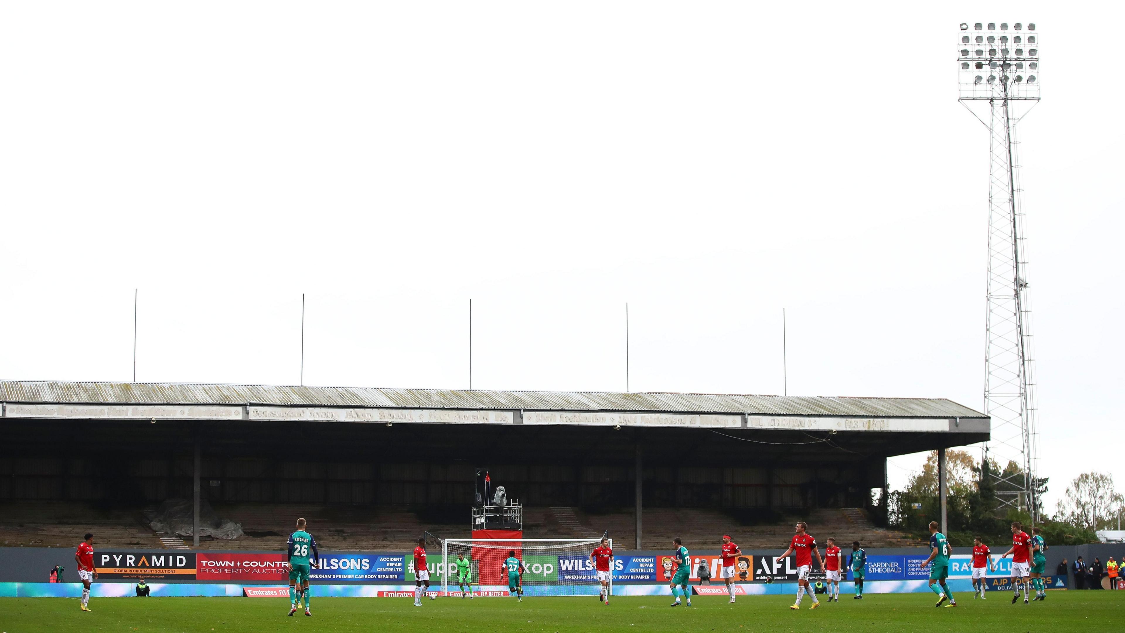 A wide lens picture of the disused Kop at Wrexham's Racecourse Ground during a game, prior to its demolition.