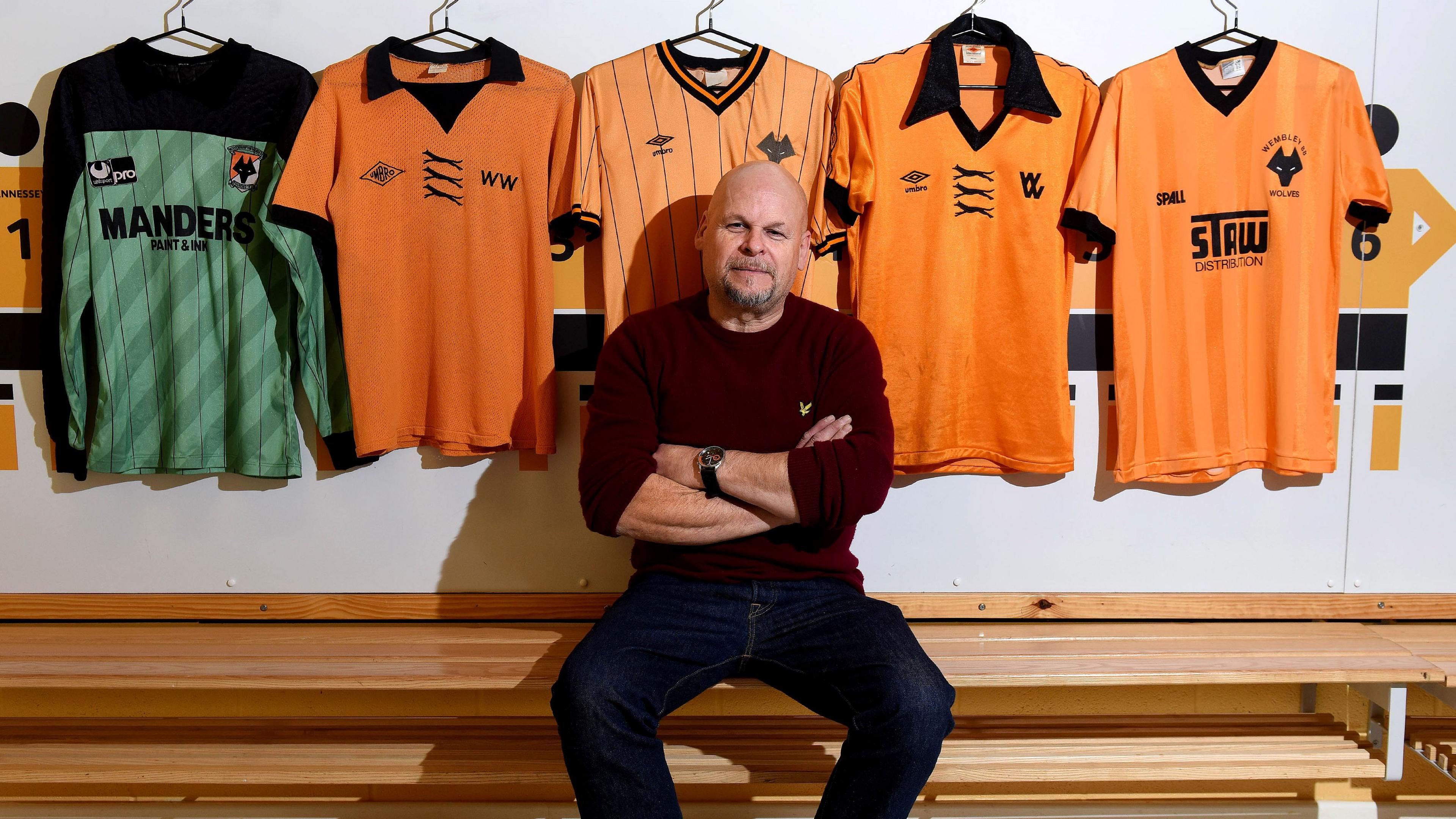 Man sat on wooden bench with five football shirts hanging behind him