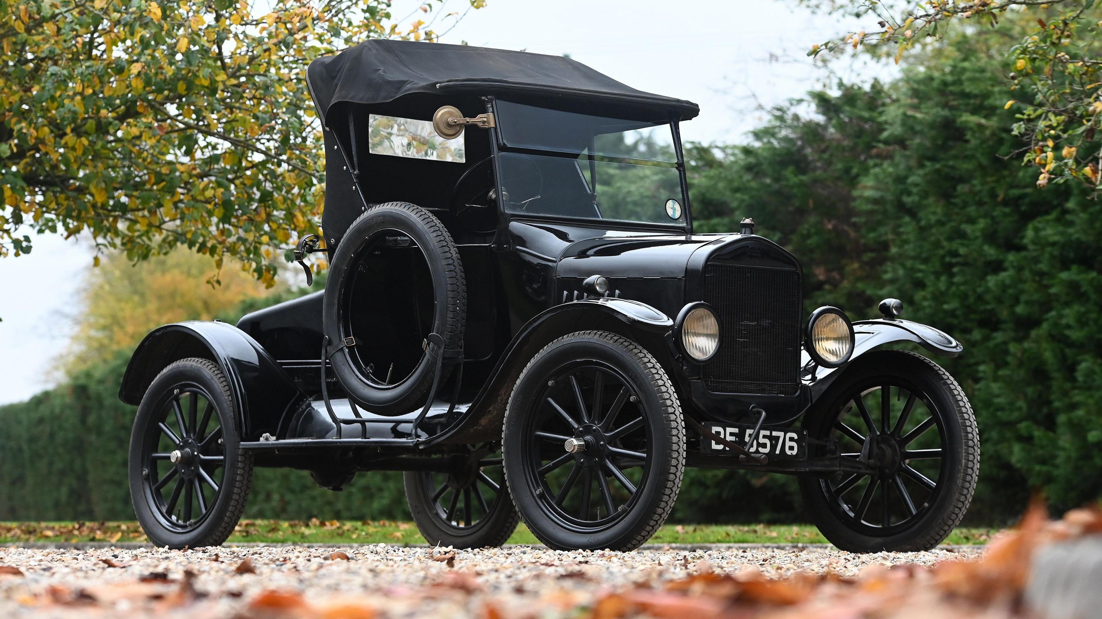 A black 1925 Ford Model T two-seat runabout being driven along a windy shingle driveway in the countryside