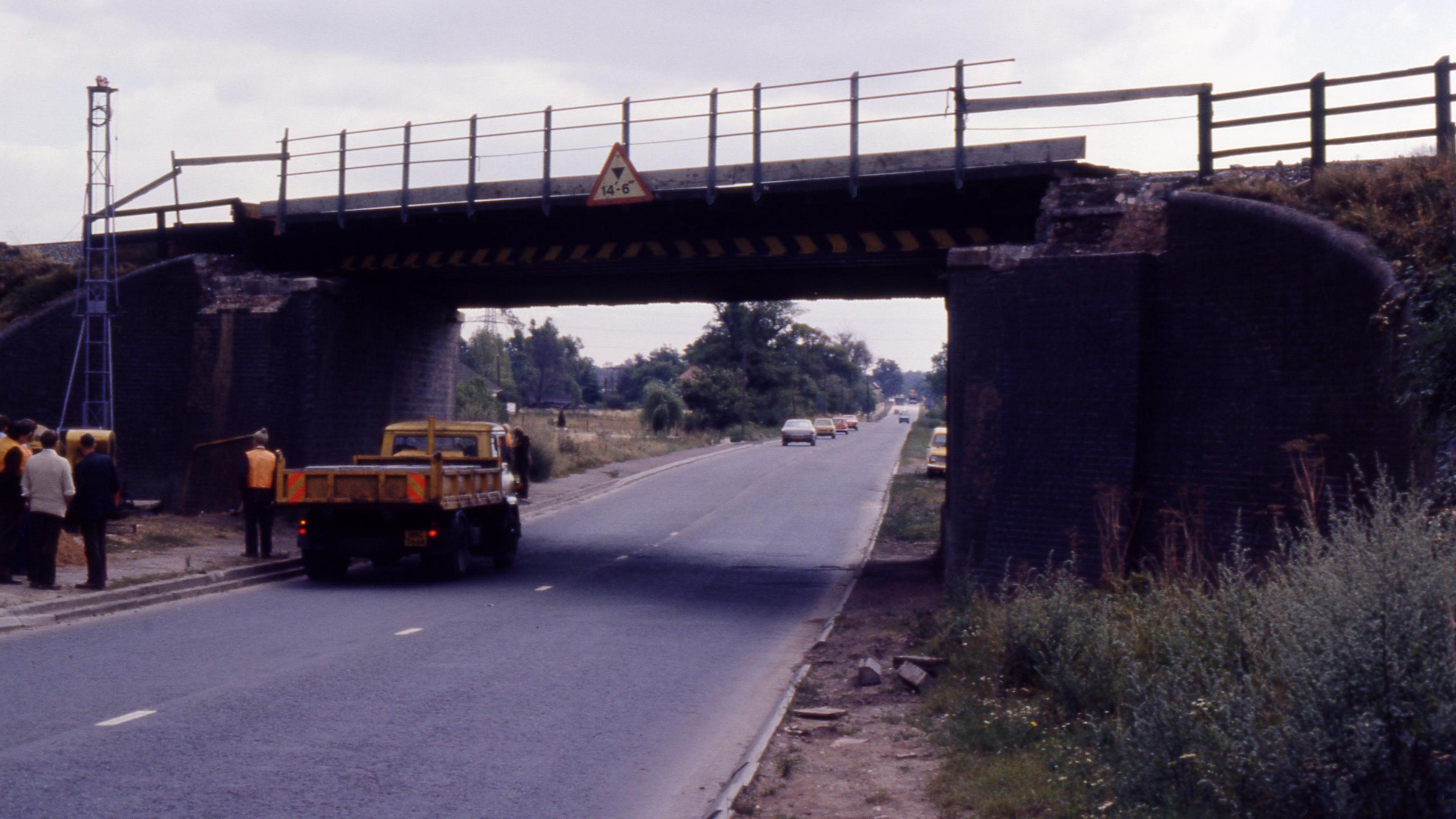 The picture from 1975 shows the A5 bridge at Hinckley as a temporary repair is made. Engineers and other railway workers are on the left side of the picture alongside a lorry. 