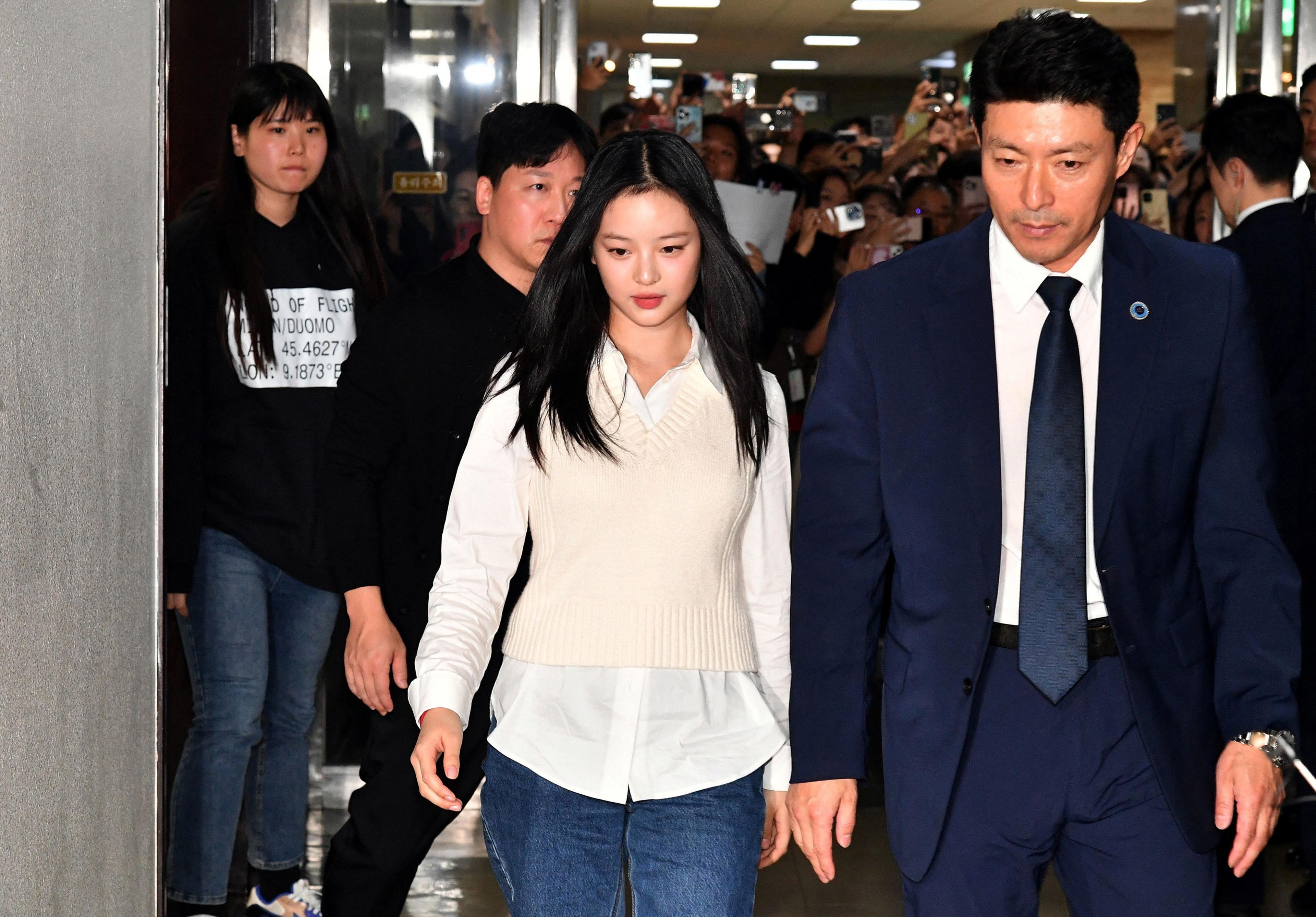 NewJeans singer Hanni arrives to testify at the National Assembly for a hearing on October 15, 2024, in Seoul, South Korea. she is wearing a white shirt, blue jeans and a cream woollen vest-top