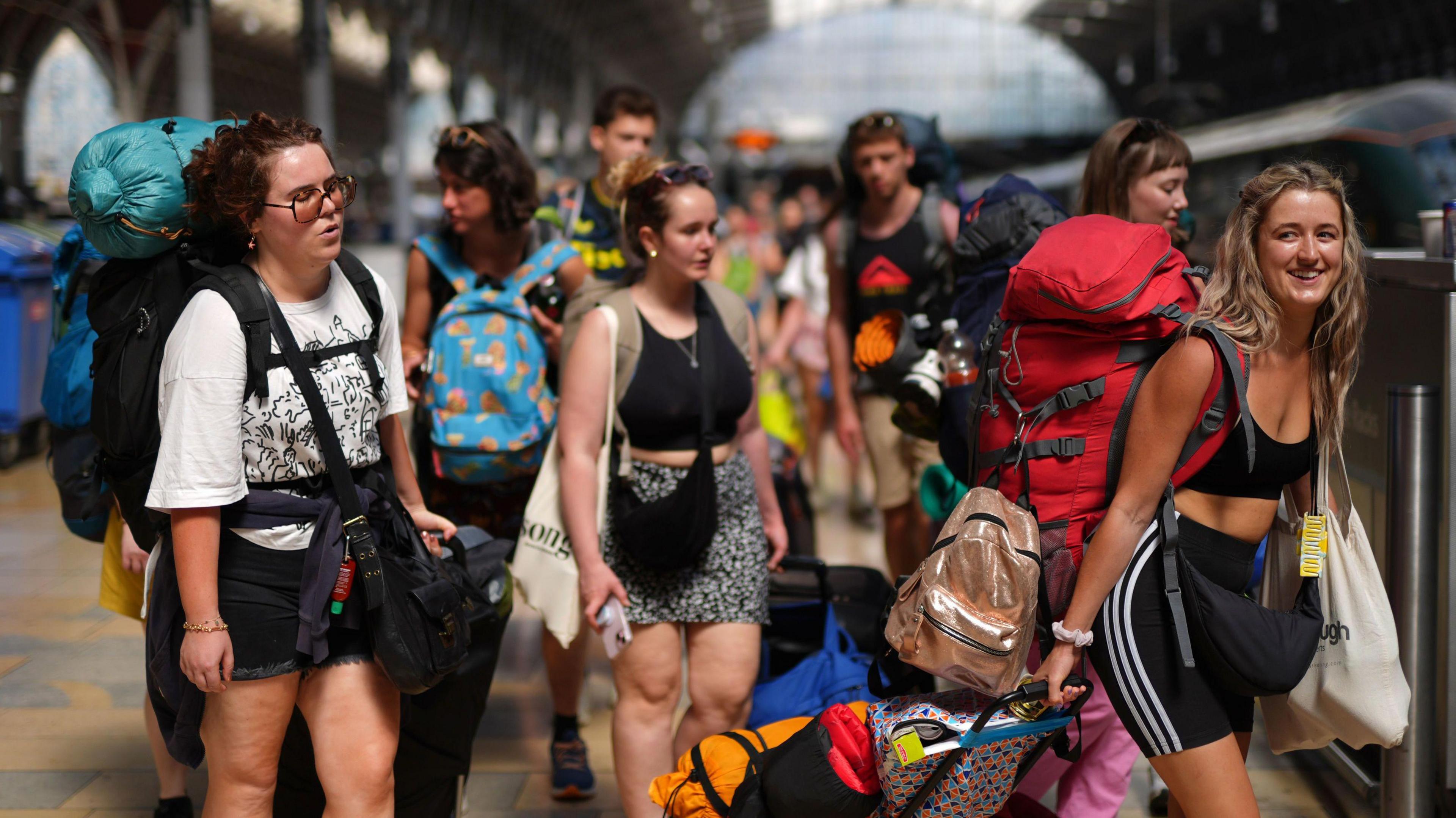 A group of people carrying large backpacks and trolleys board a train at London Paddington. 