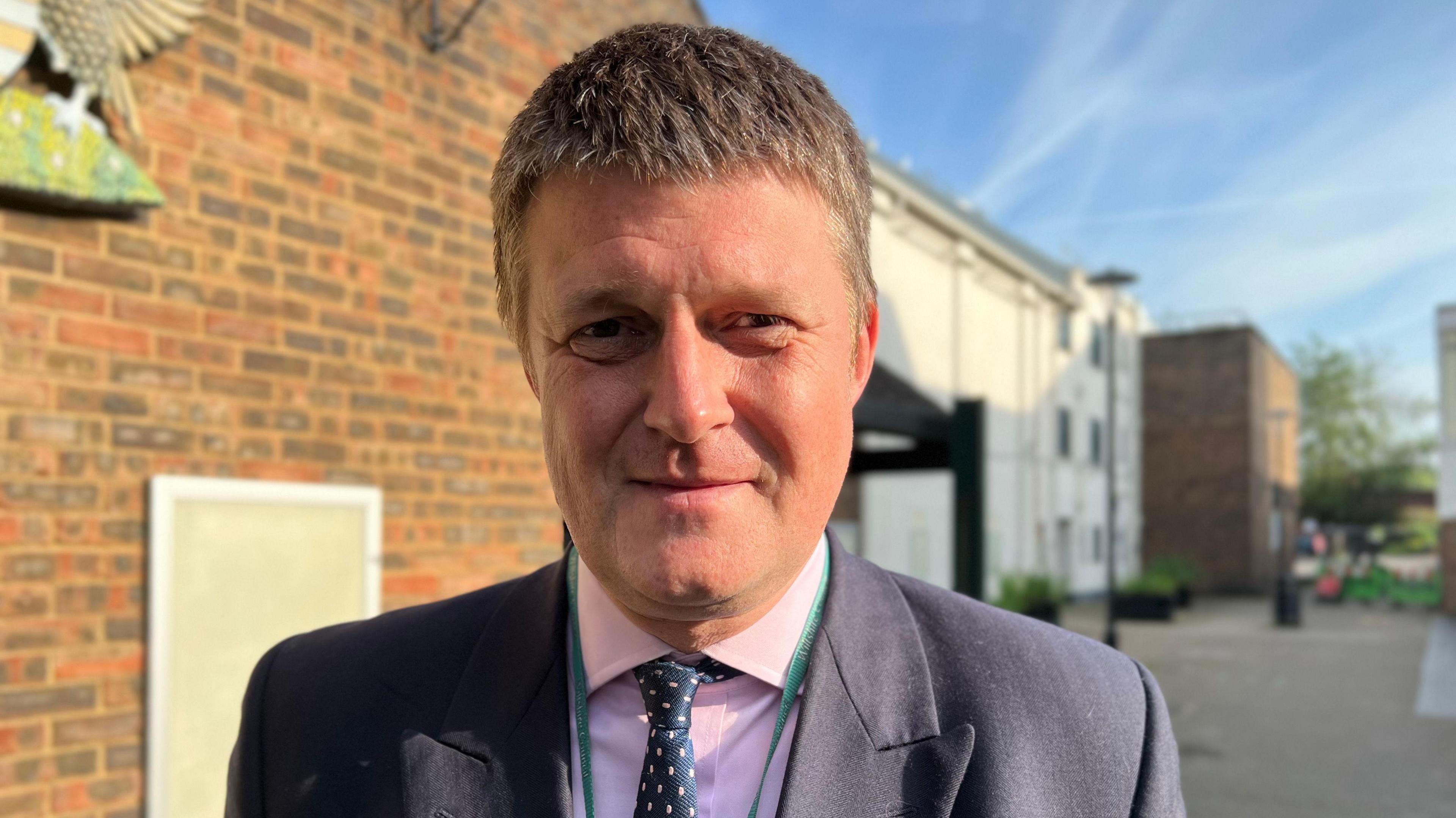 A photo showing the leader of Wiltshire Council, Richard Clewer, dressed in a blue suit and wearing a tie