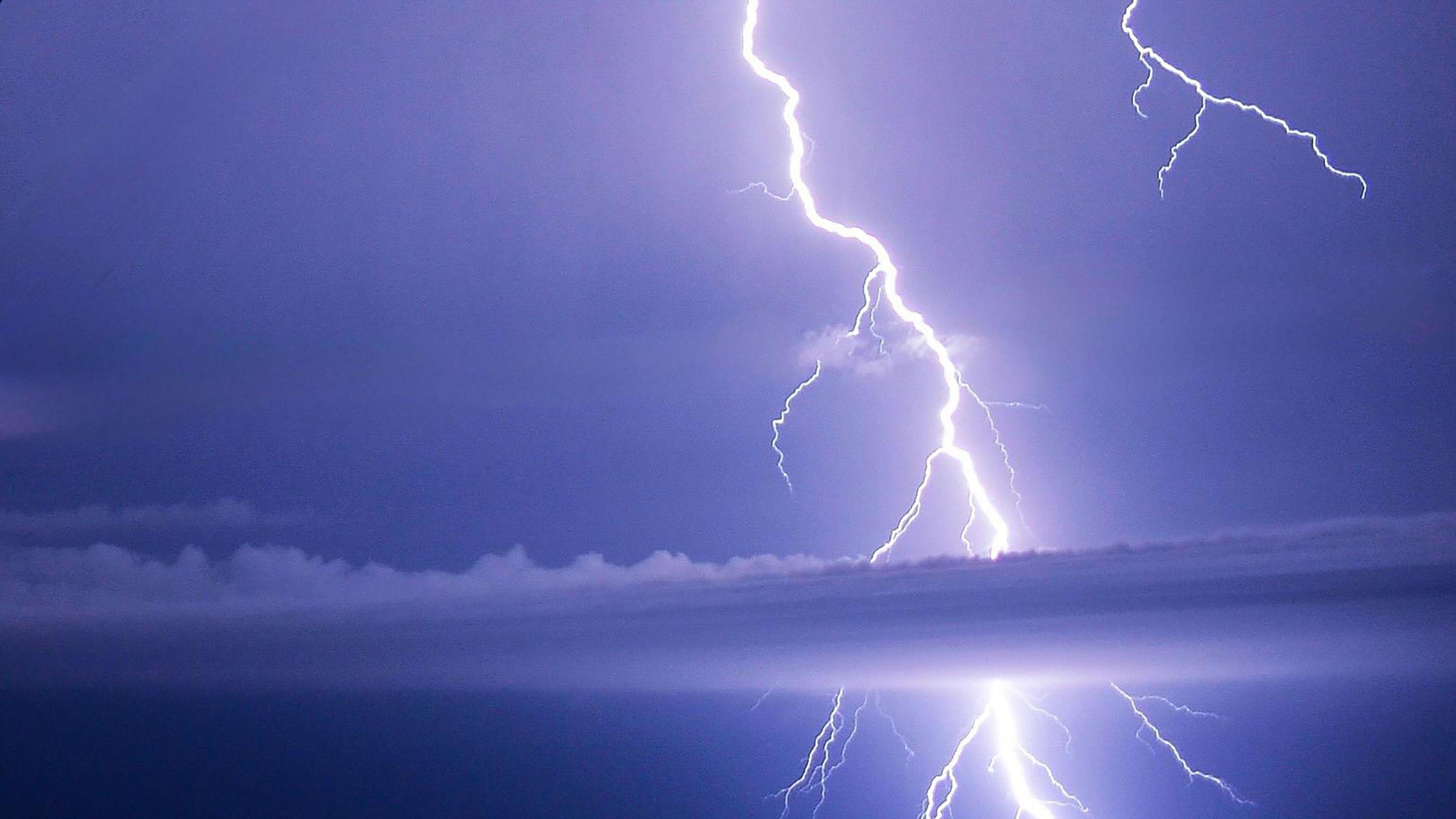 A white bolt of lightning illuminates a purple sky, with a thin, white cloud in the foreground.