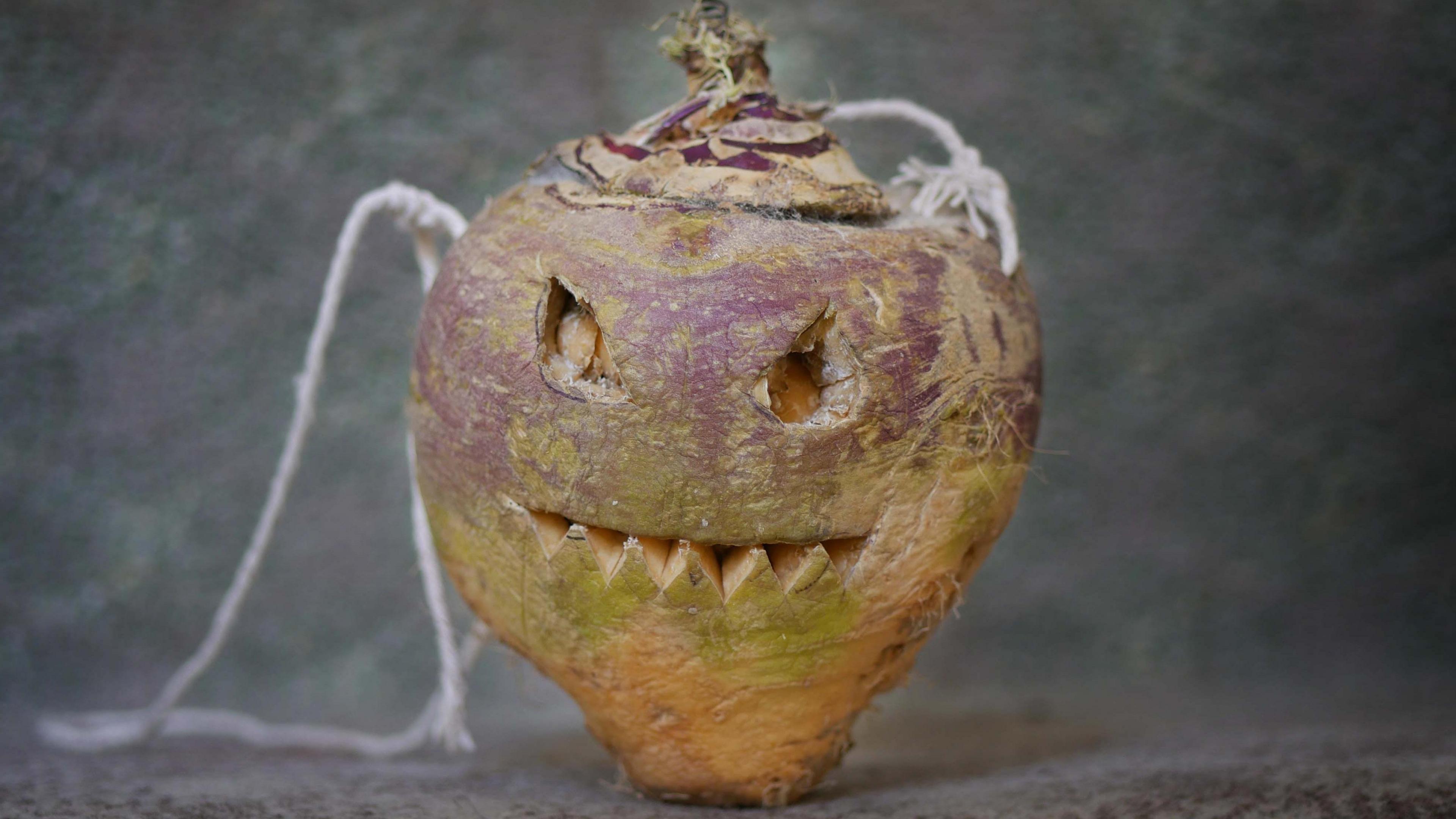 A turnip carved with a spooky face carved in the style of a pumpkin, with string attached for carrying. 