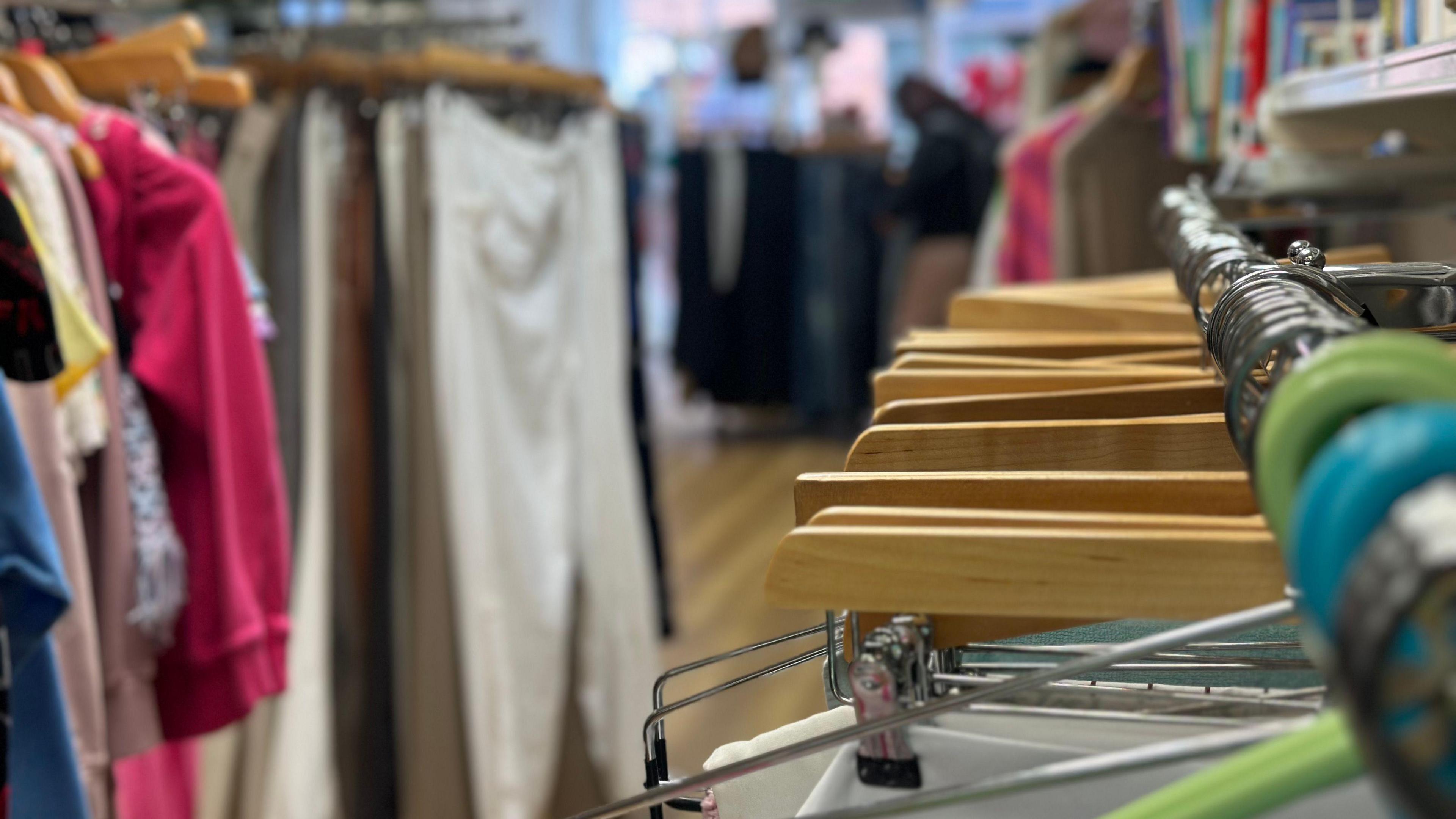 A clothes rail in the foreground with coloured clothes hangars in a charity shop