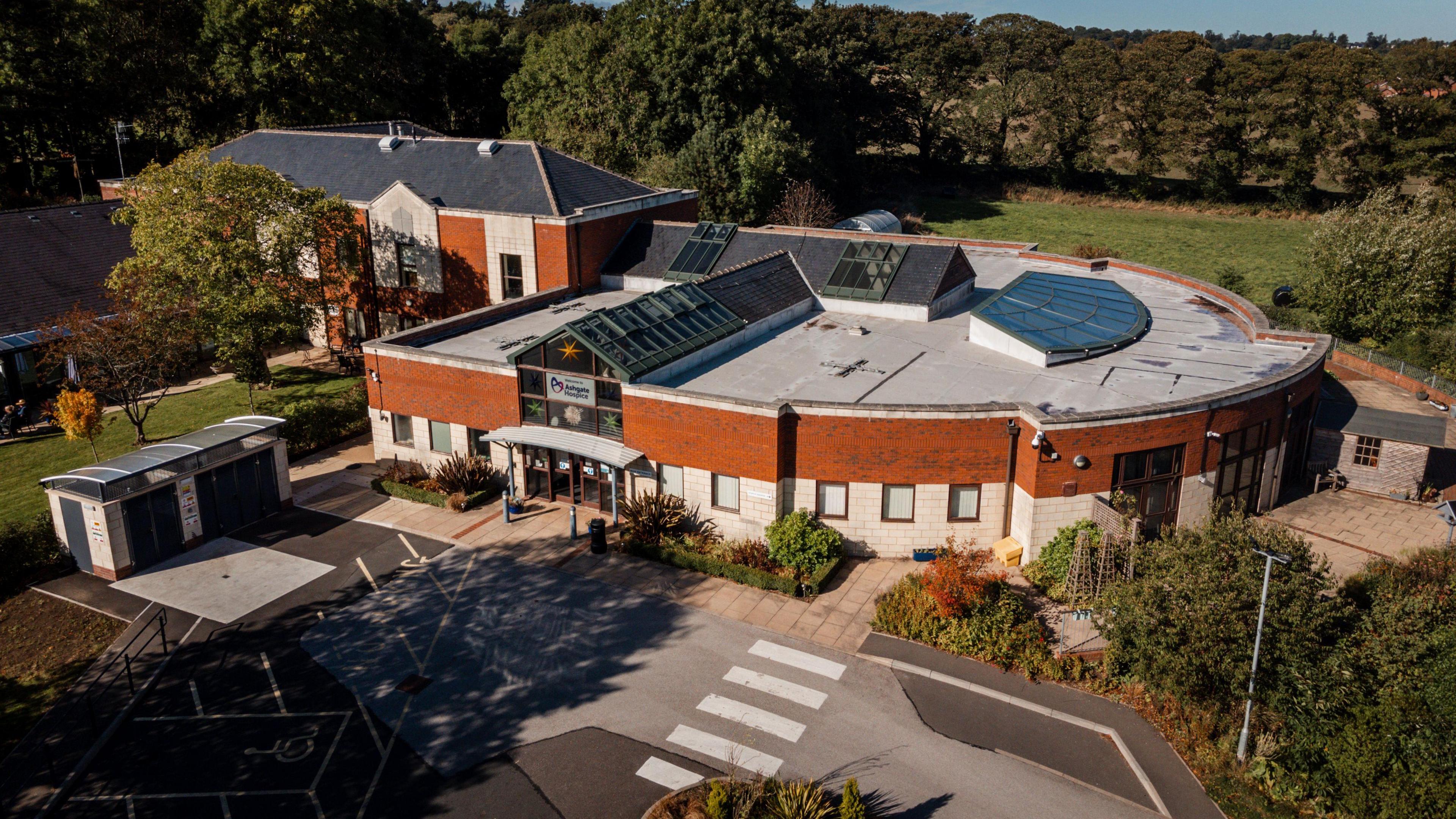 A drone image of Ashgate hospice. It is shaped in a semi circle with trees around the perimeter of the grounds.