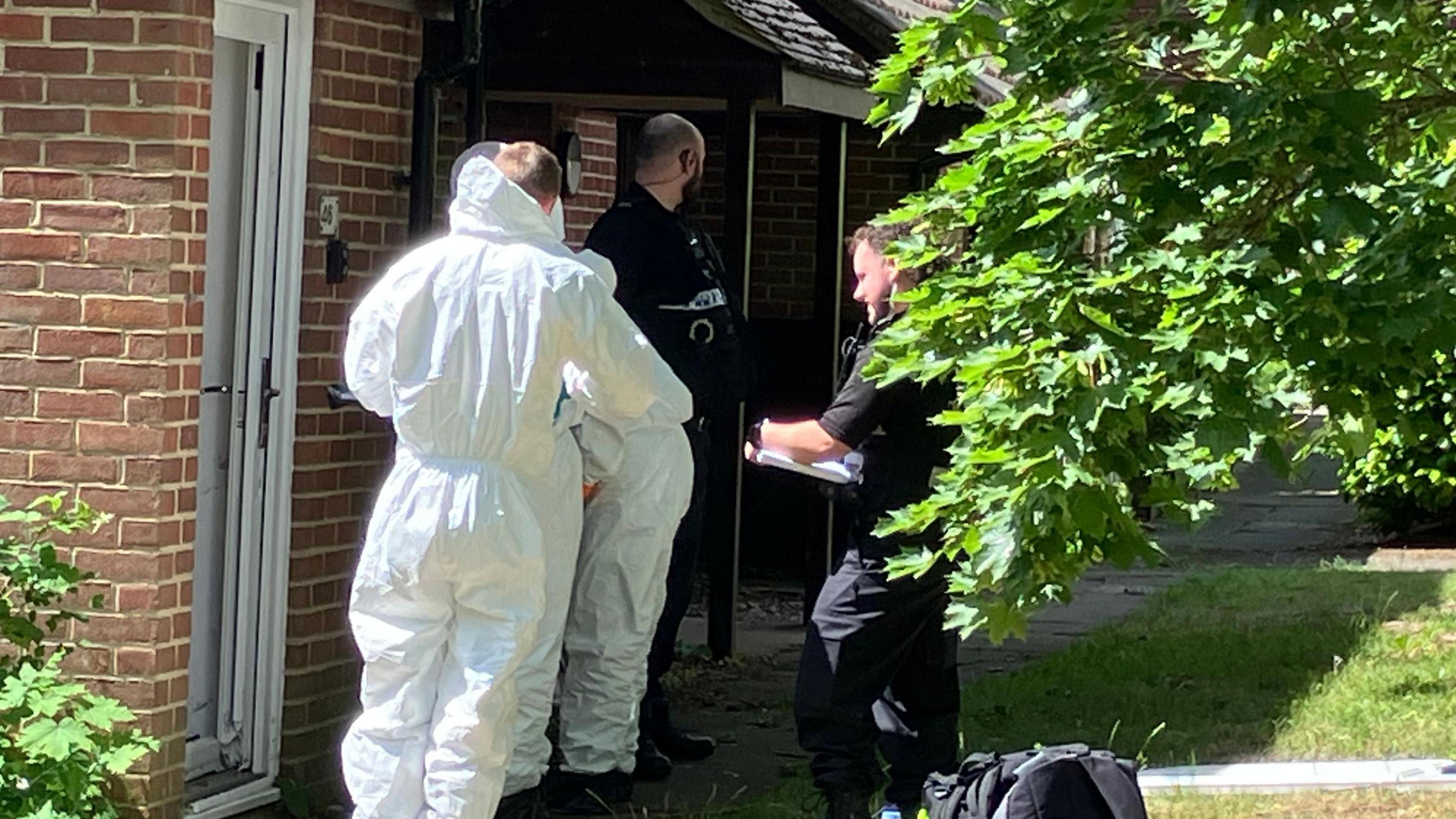 Forensic officers and police officers stood outside of a brick property.