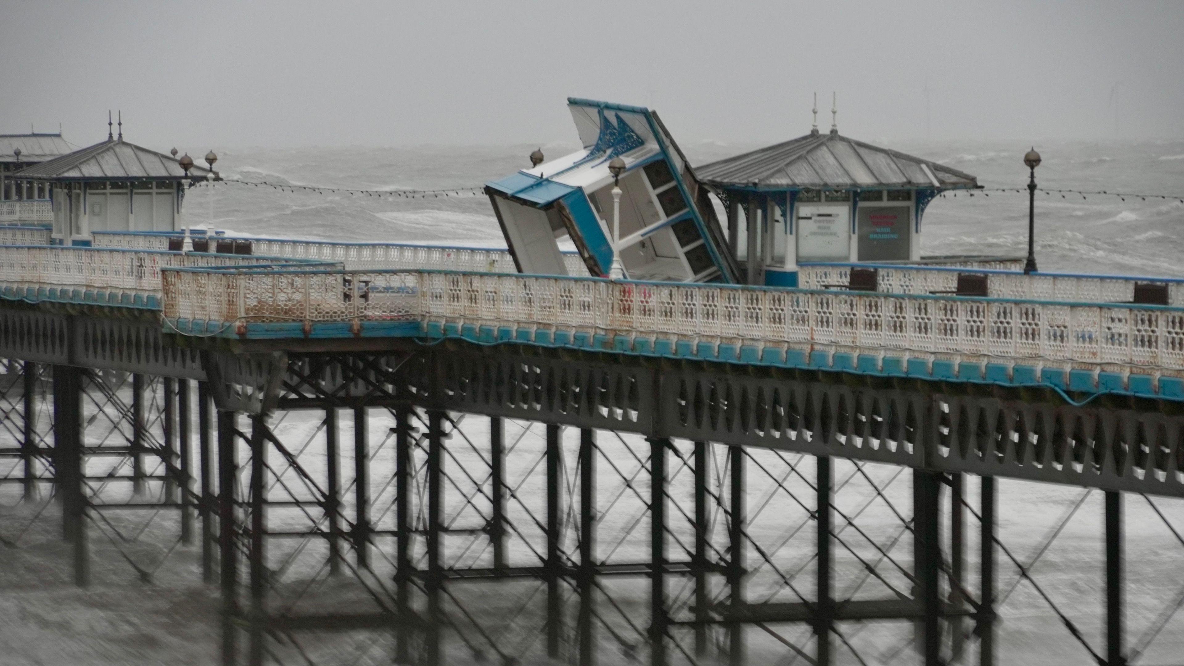 A white and blue wooden unit on Llandudno Pier appears on its side amid a gloomy and stormy backdrop 