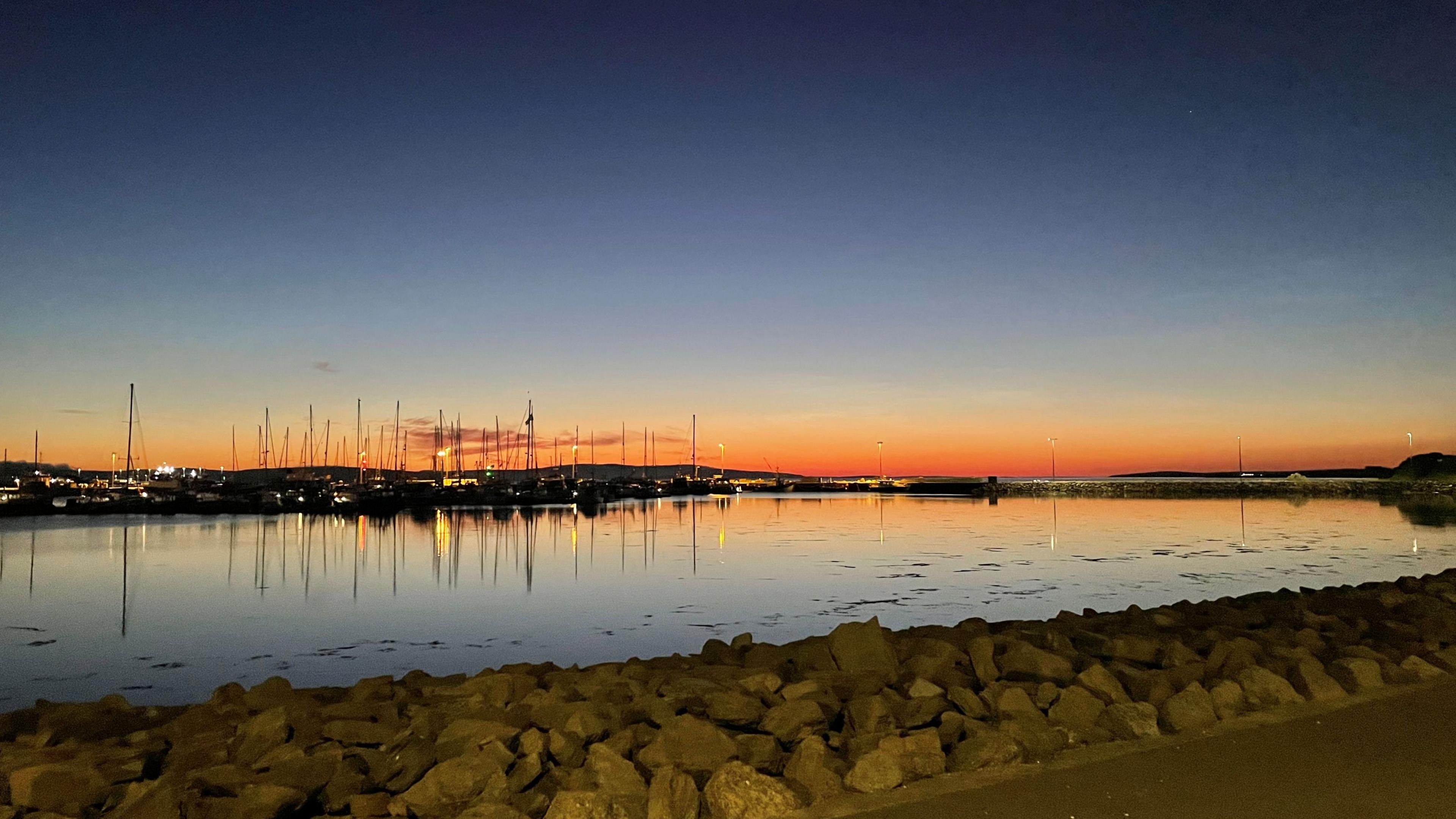 A sunset glistens over a marina in Orkney