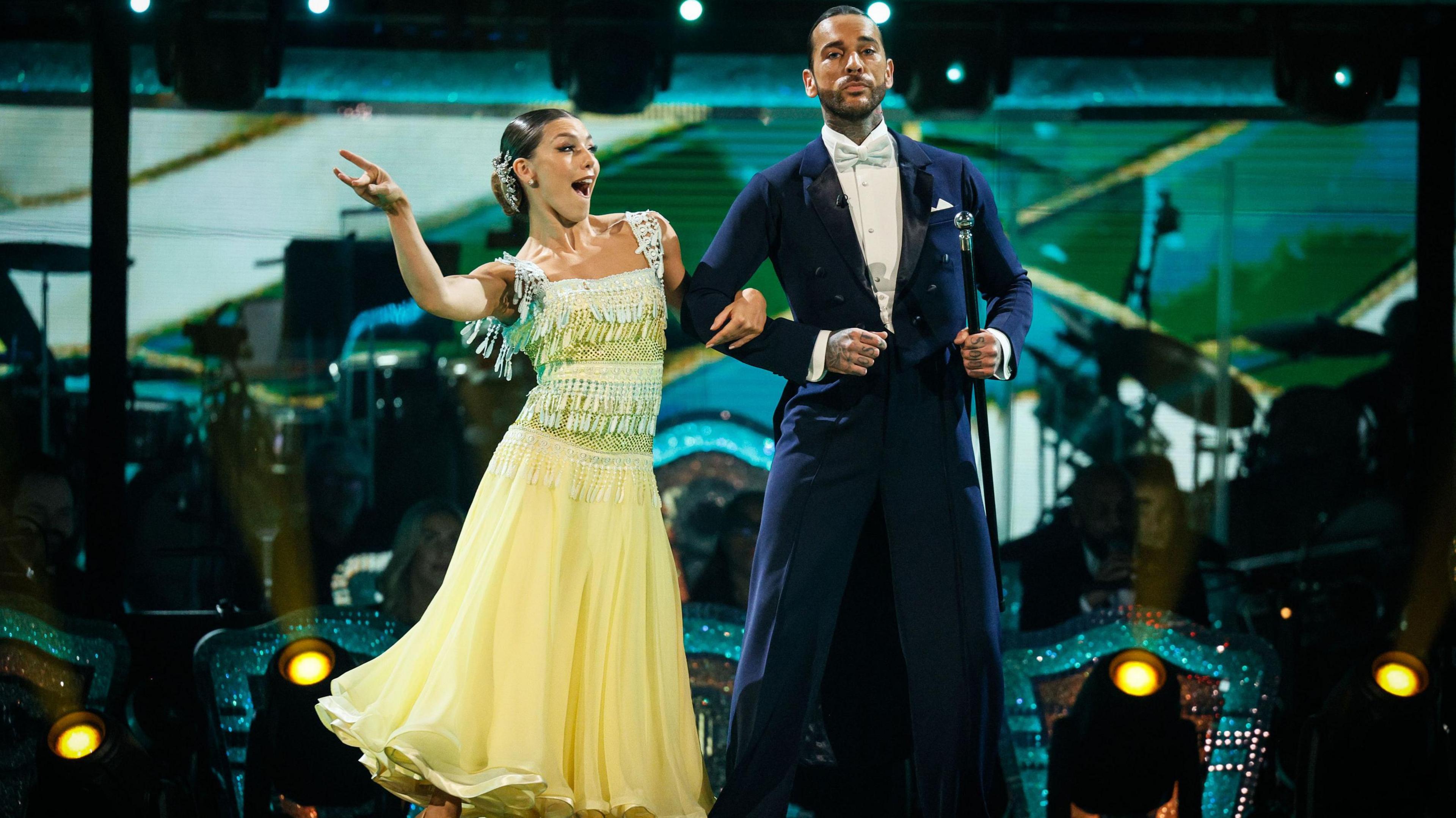 Pete and Jowita dance - she is wearing a yellow floaty dress and he wears a traditional morning suit and holds a cane.