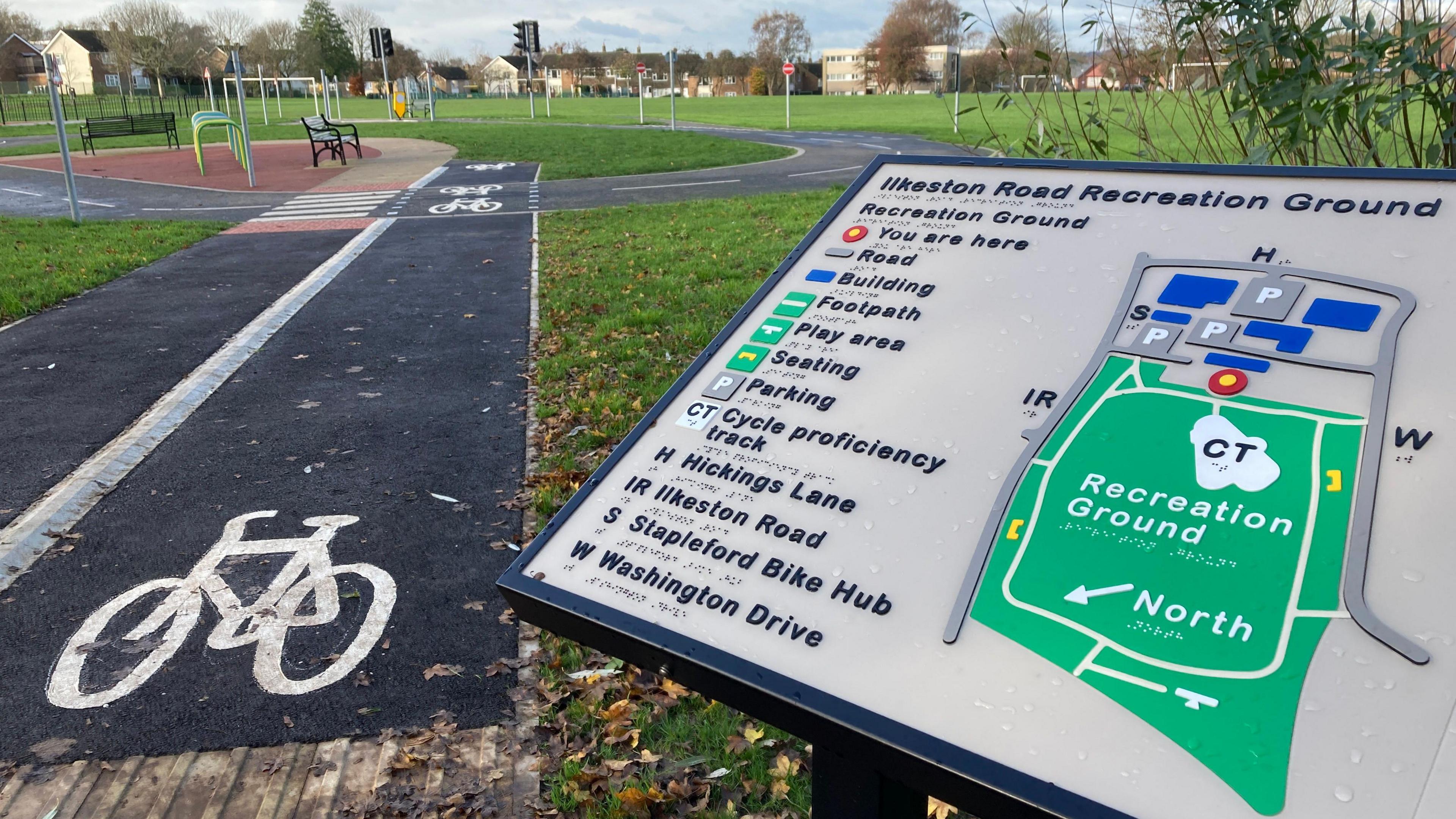 A map - with raised words and markings - showing the layout of the recreation ground, next to a path which has a kerb and bicycle lane markings.