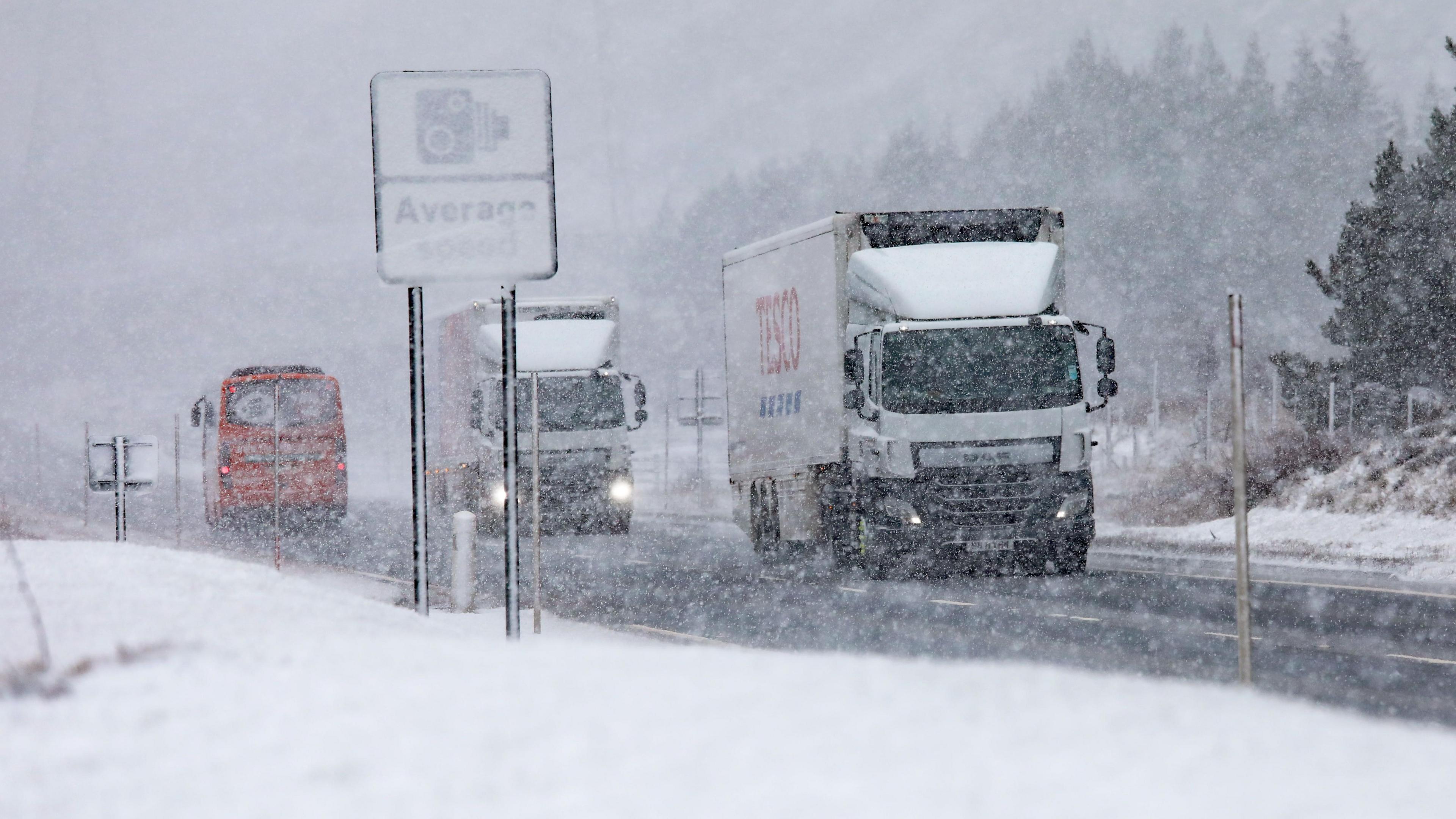 Lorries make their way along a snowy A9 with a sign for average speed cameras only just visible