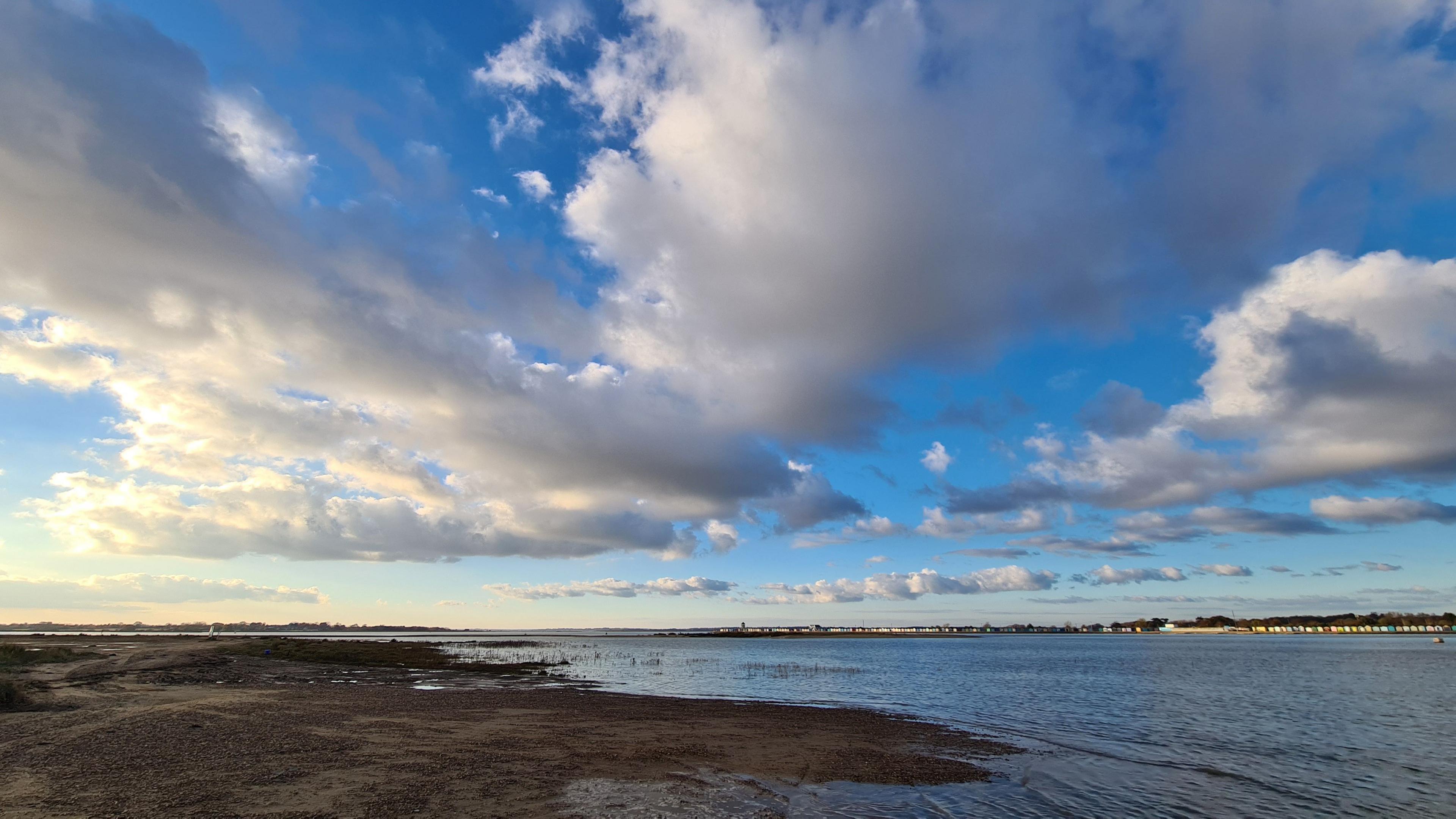 The beach at Point Clear in Essex. Above is a blue sky with white fluffy clouds, and in the distance beach huts can be seen at Brightlingsea.