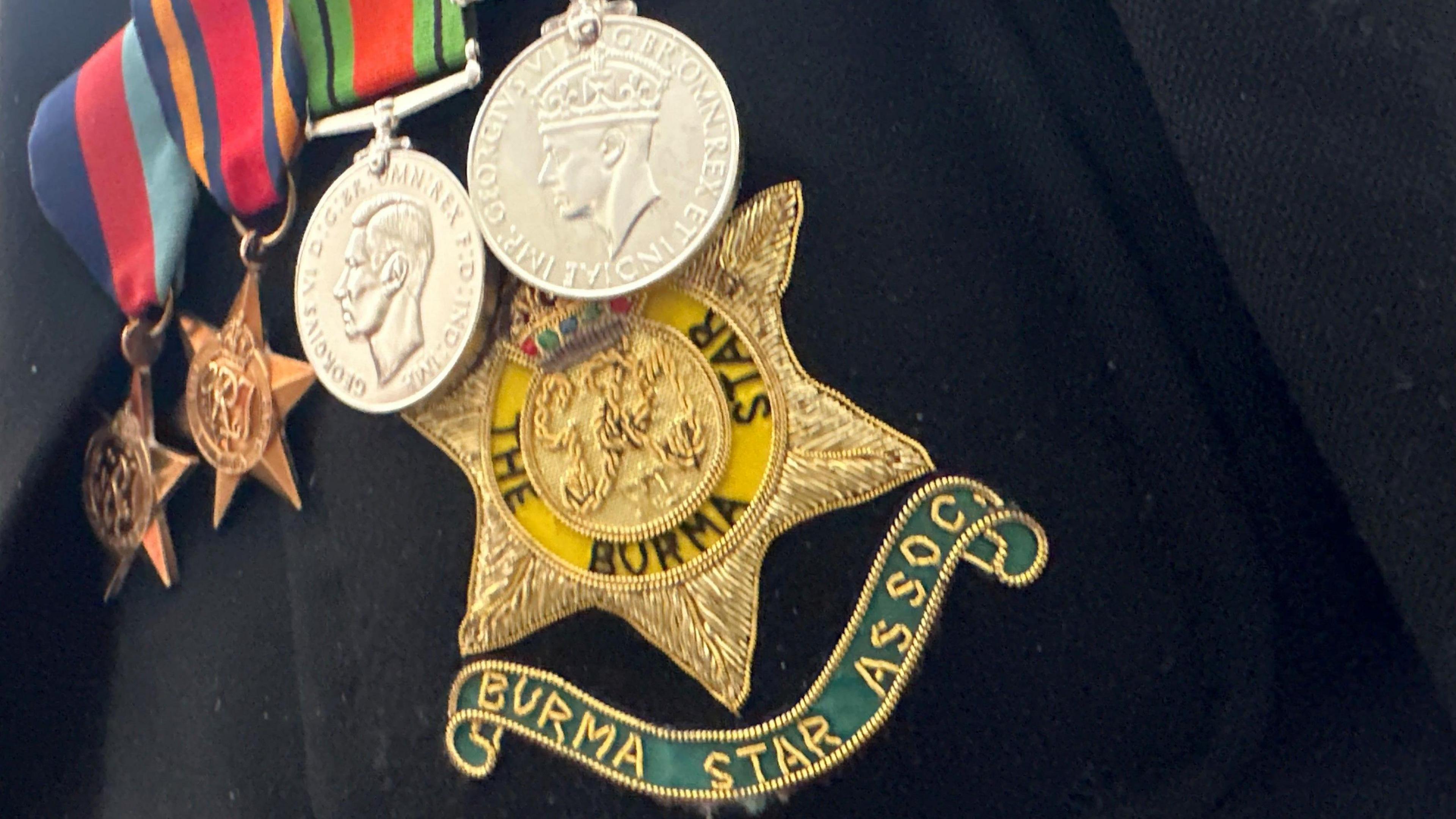 Medals pinned to a dark jacket, they are hanging on colourful stiped ribbons. There hand over the gold star of the Burma Star emblem.
