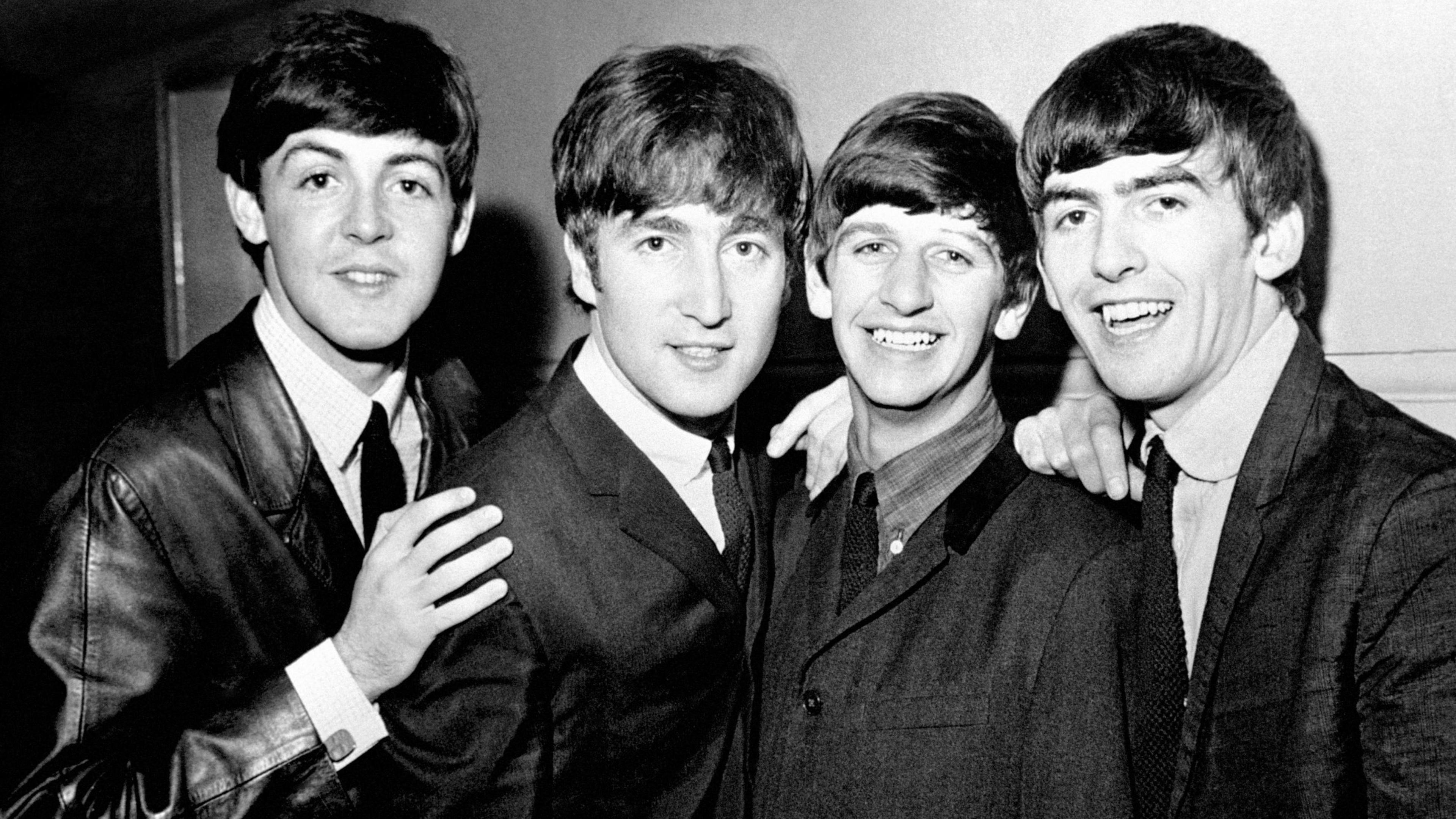 A black and white image of Paul McCartney, John Lennon, Ringo Starr and George Harrison taken in 1963. The men are all in black jackets, shirts and ties.