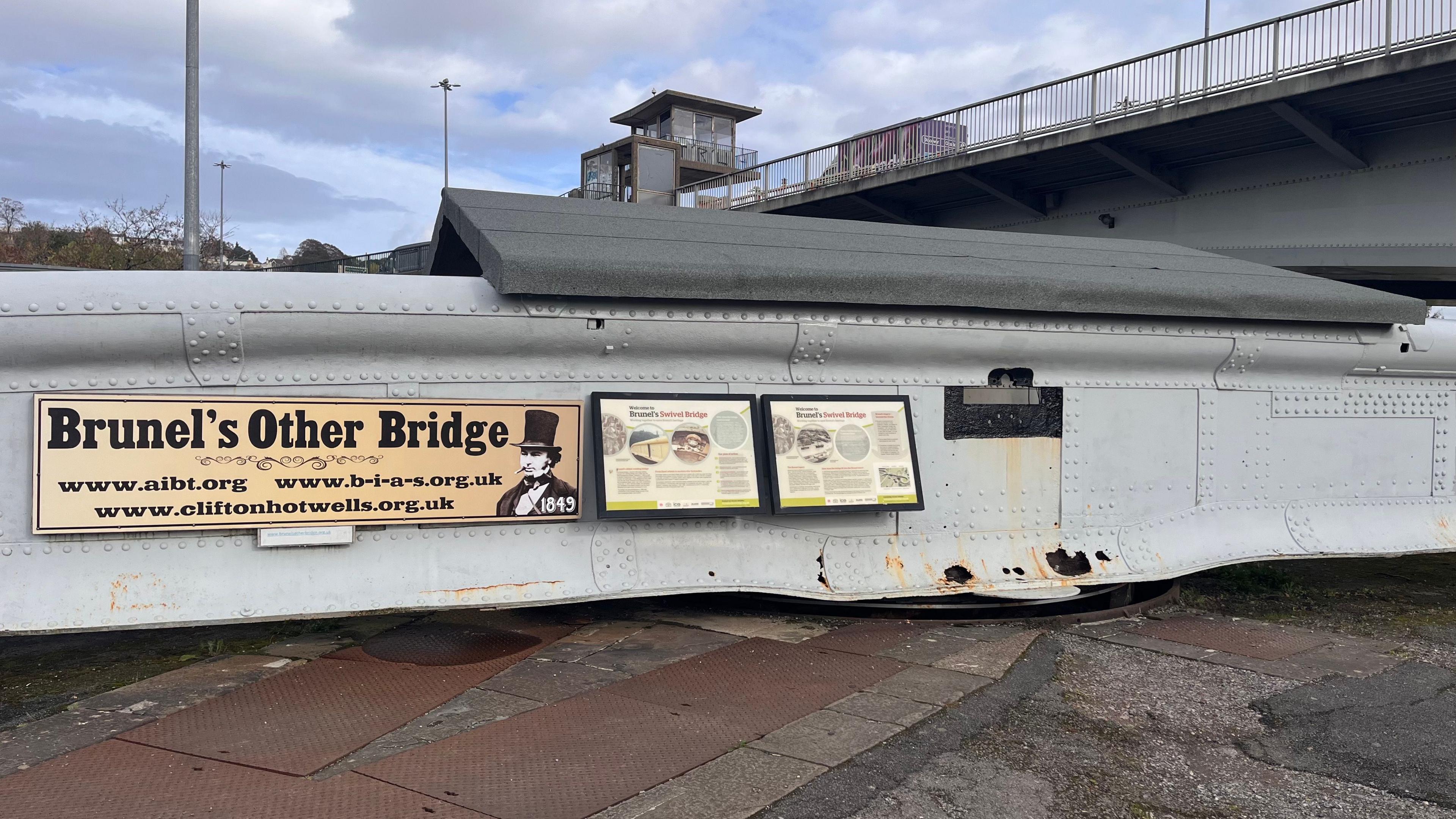The photo shows Brunel's Other Bridge in the present day. Two information boards detailing the bridge's history can be seen on its side. The Pimsoll Bridge which replaced it, can be seen in the background. 