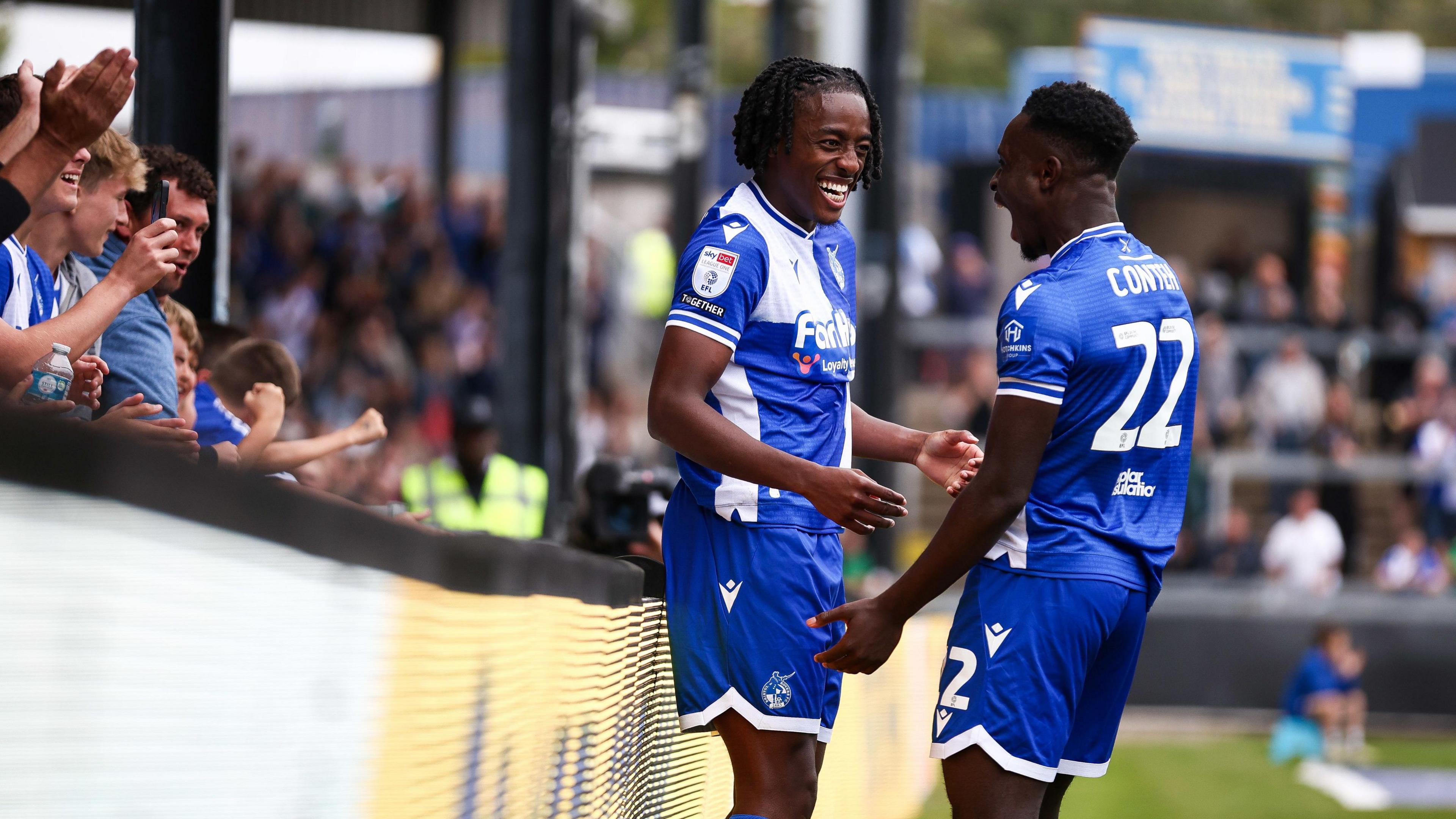 Two Bristol Rovers players celebrate a goal during their 2-0 win over Cambridge United at the Memorial Stadium. Fans are seen applauding on the left of the picture