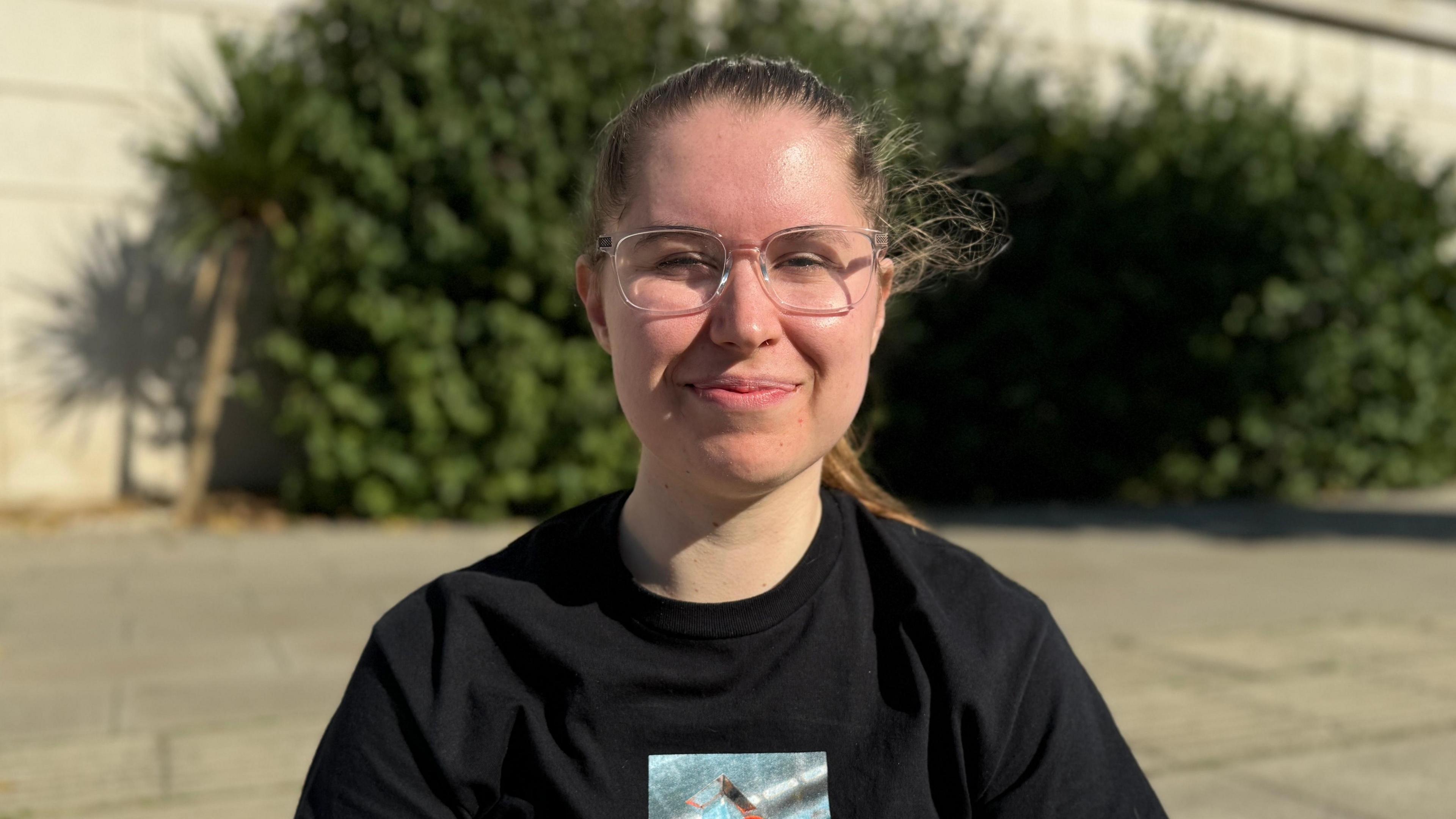 Female student with tied back brown hair sat in Nottingham city centre wearing a black t shirt and glasses