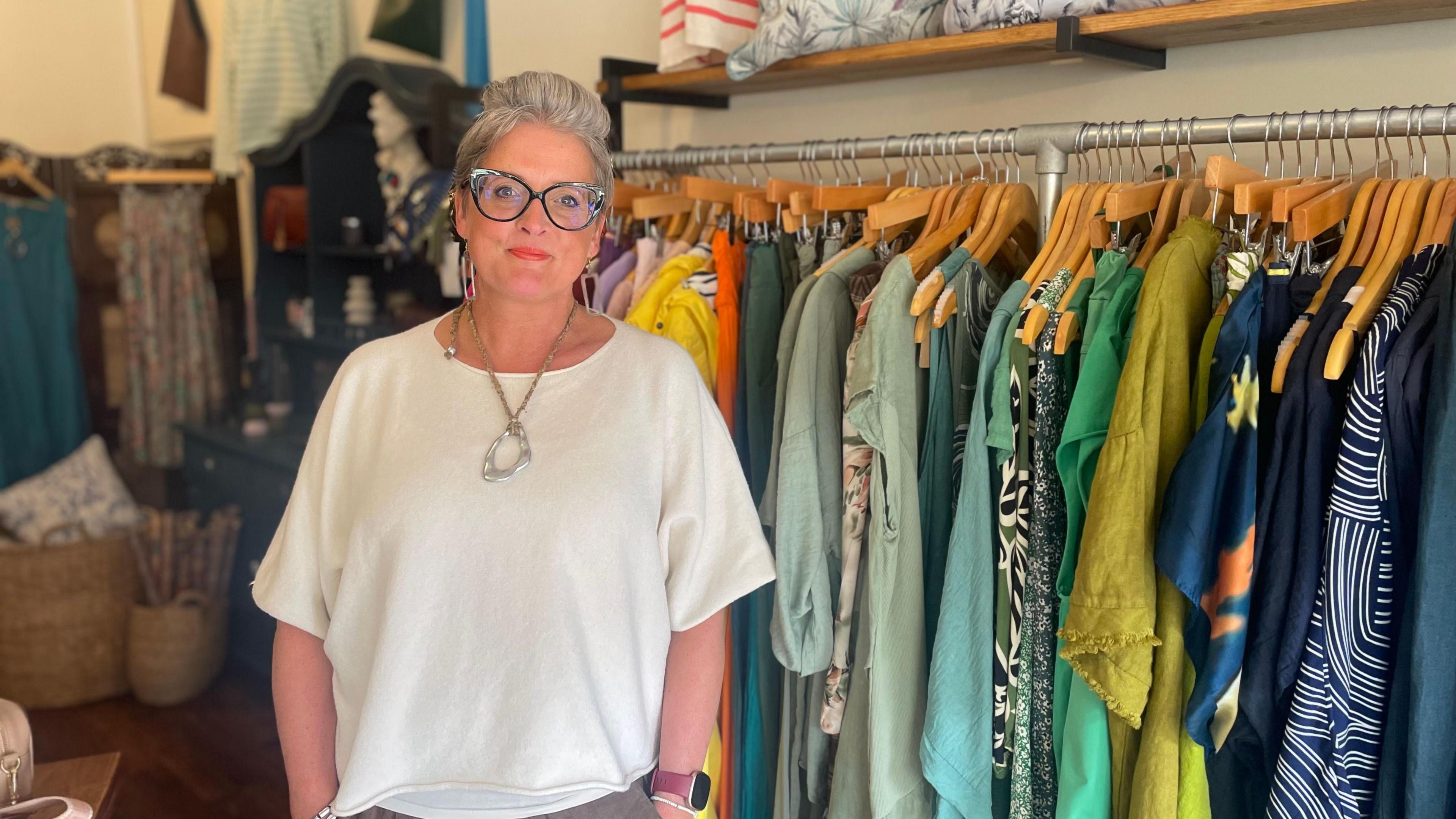 Shop owner stood in front or railing of colourful clothes