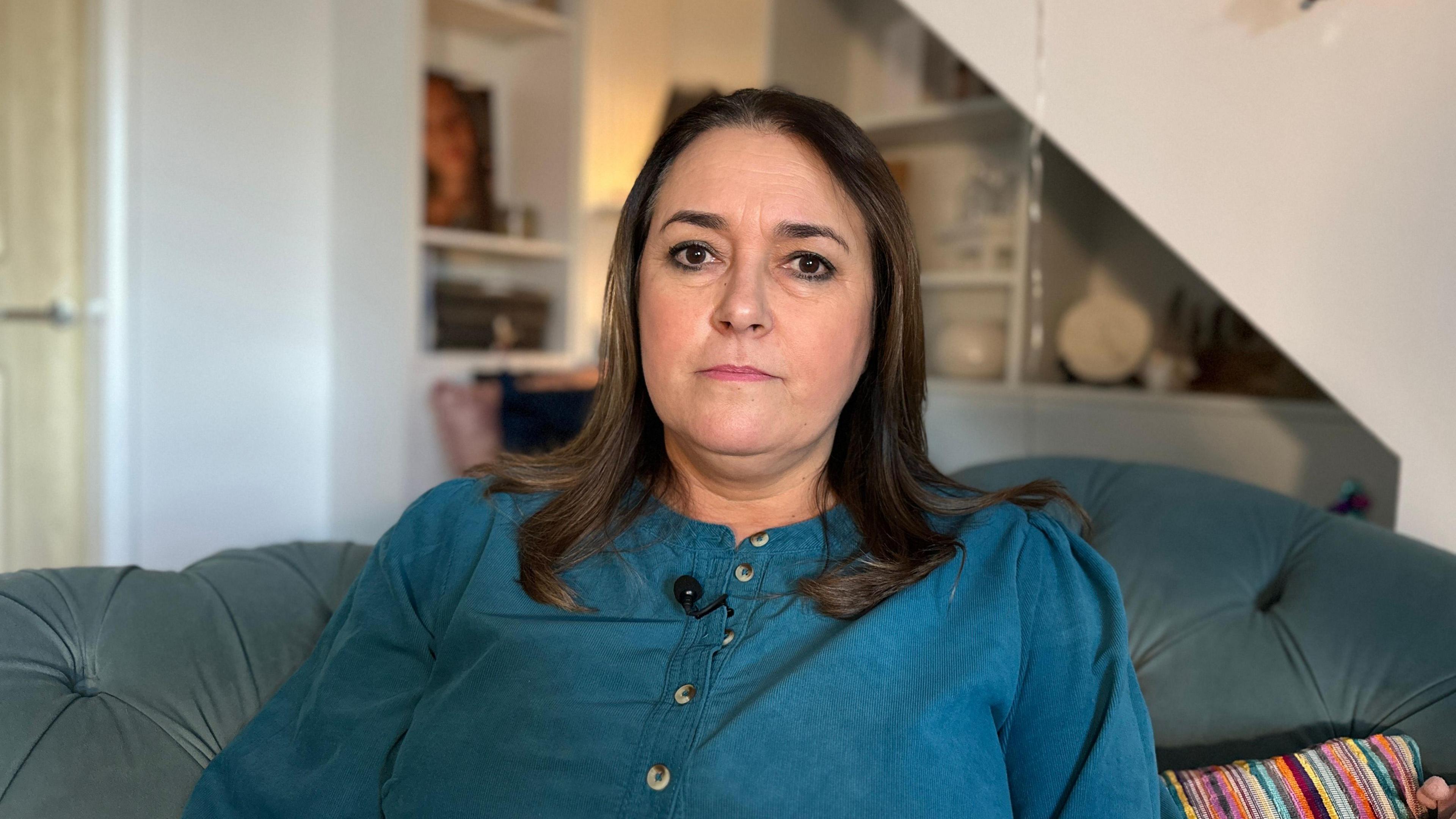 Nicky Johnson sitting on a sofa wearing a blue top. She has dark hair.