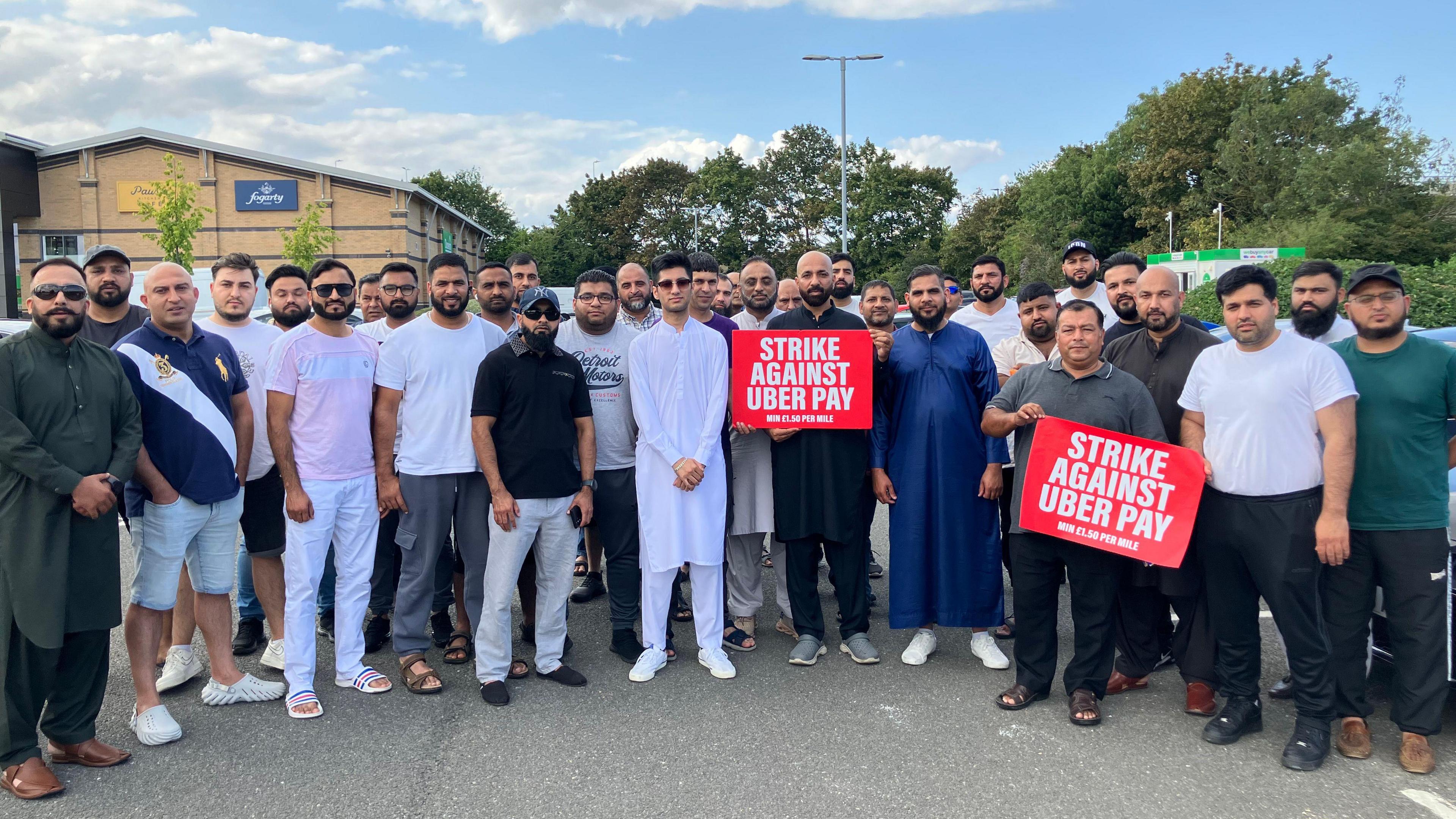 A group of drivers standing in a semi-circle at Maskew Avenue Retail Park - some holding red strike signs.