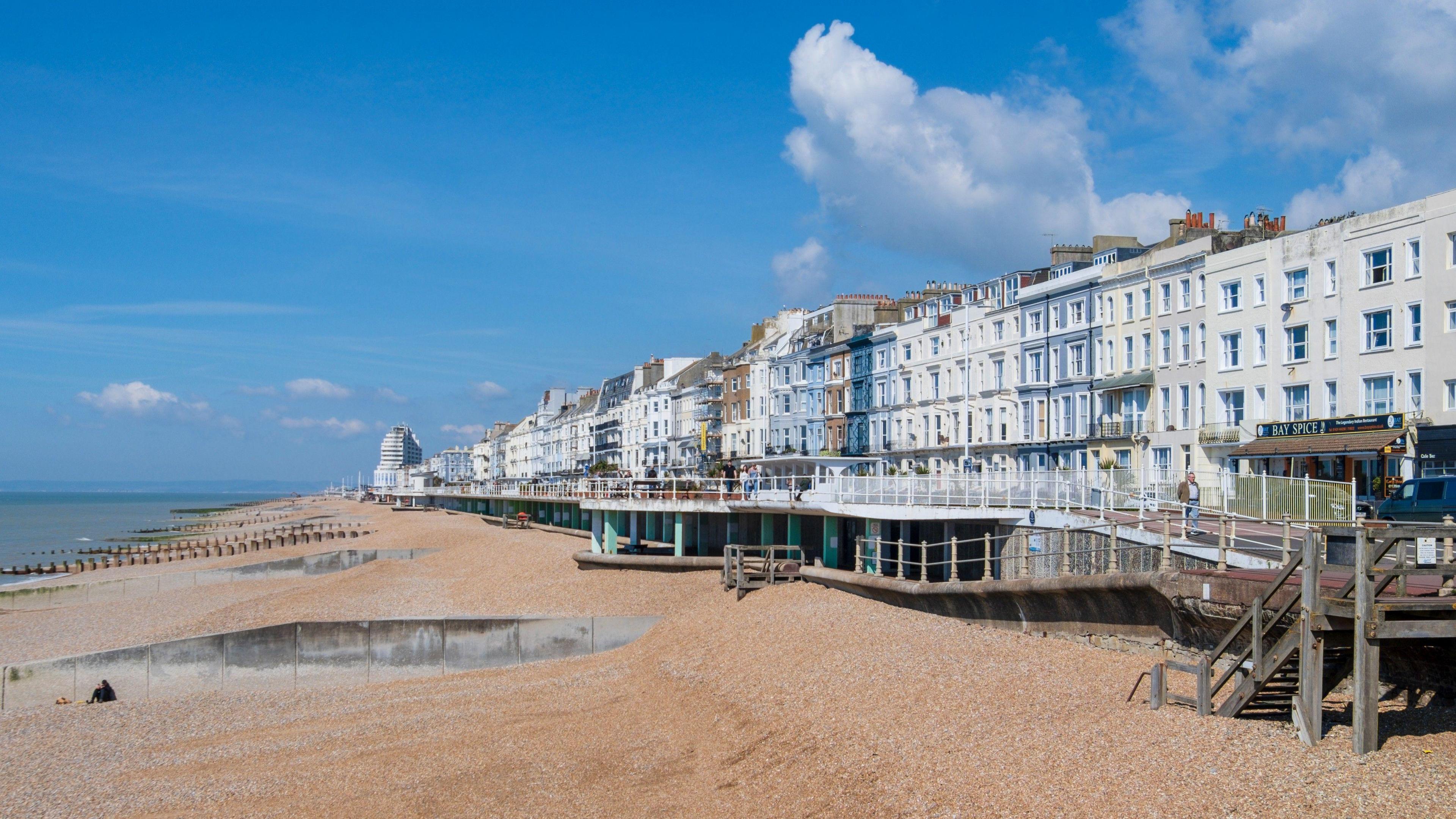 A view of Hastings seafront, featuring its shingle beach, promenade and Victorian terrace buildings.