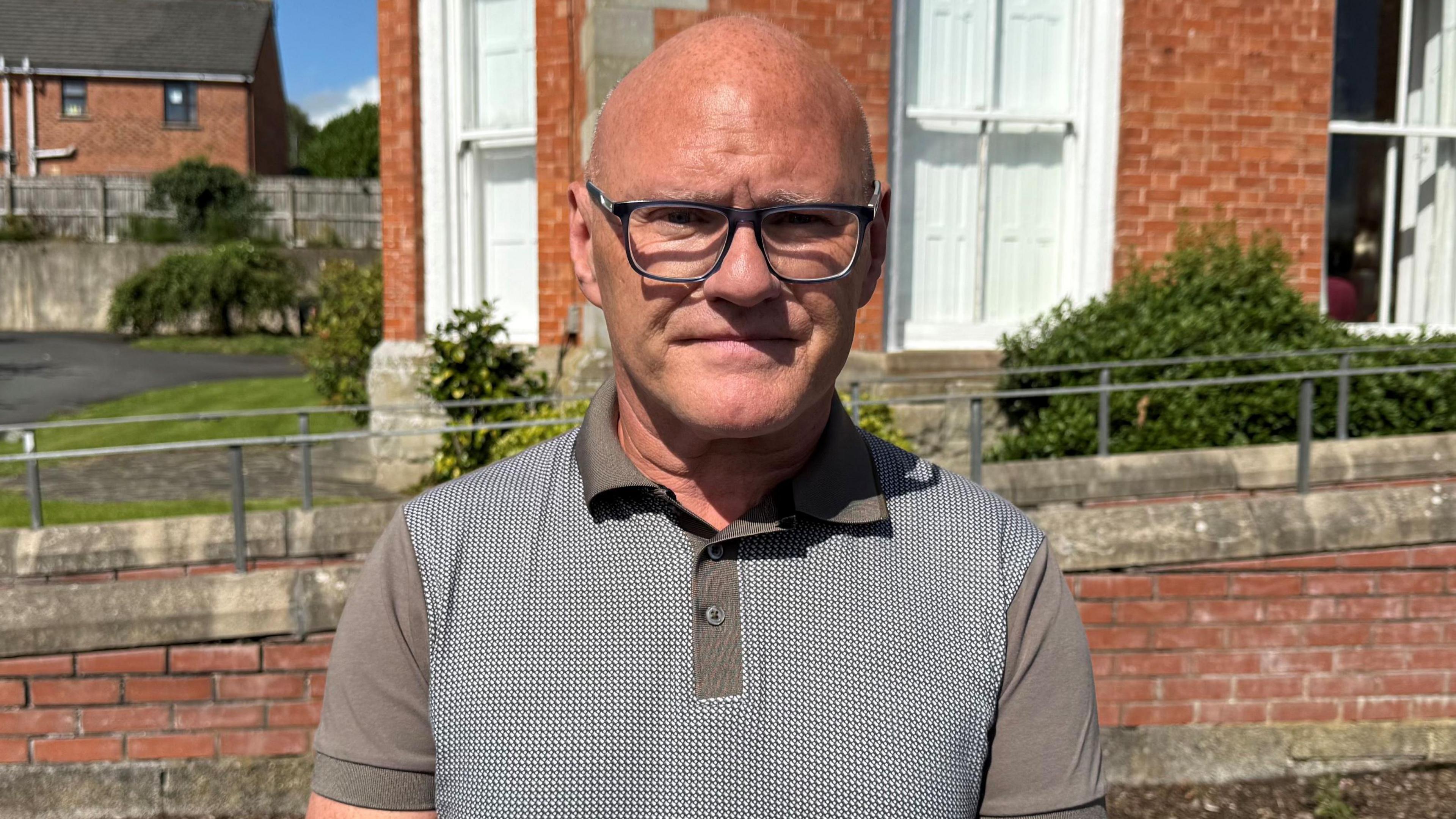 Paul Maskey wearing a green polo with check design, he wears glasses. 