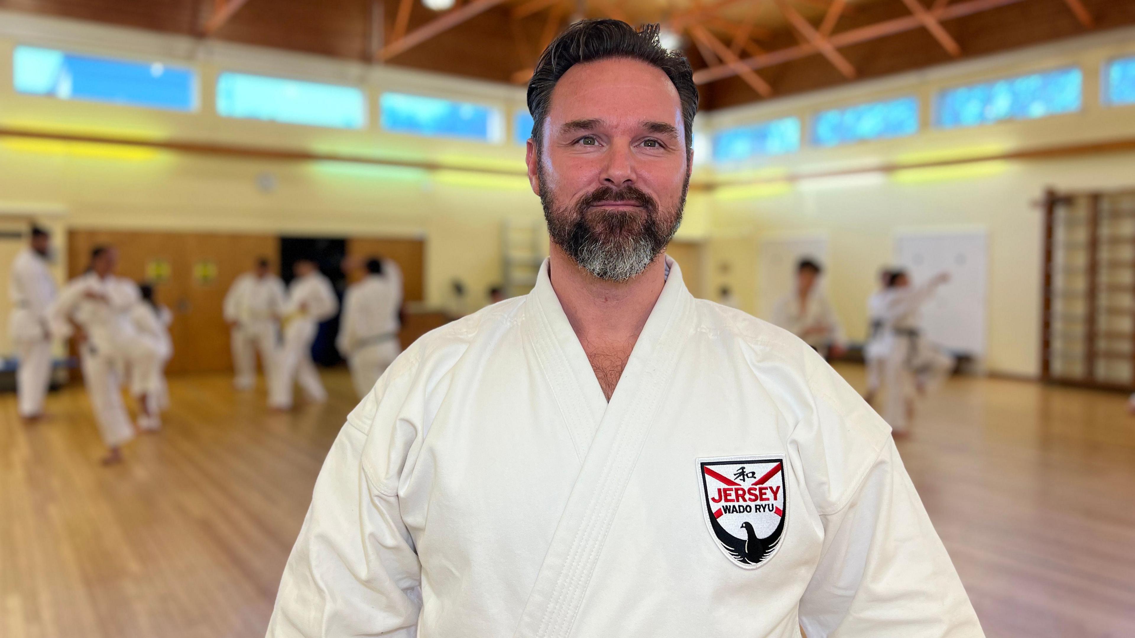 Karate coach Ryan Lambotte looks at the camera while his class practices in the background