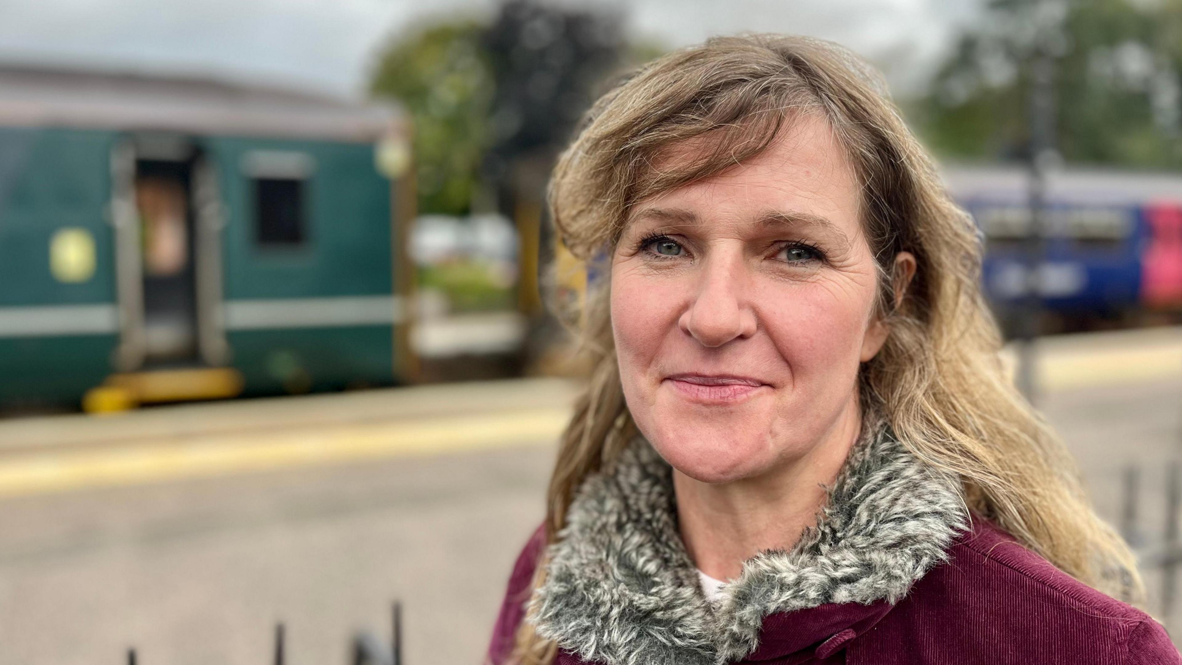 Bryony Chetwode wearing a jacket with a fur collar standing in front of the platform at Crediton Railway Station