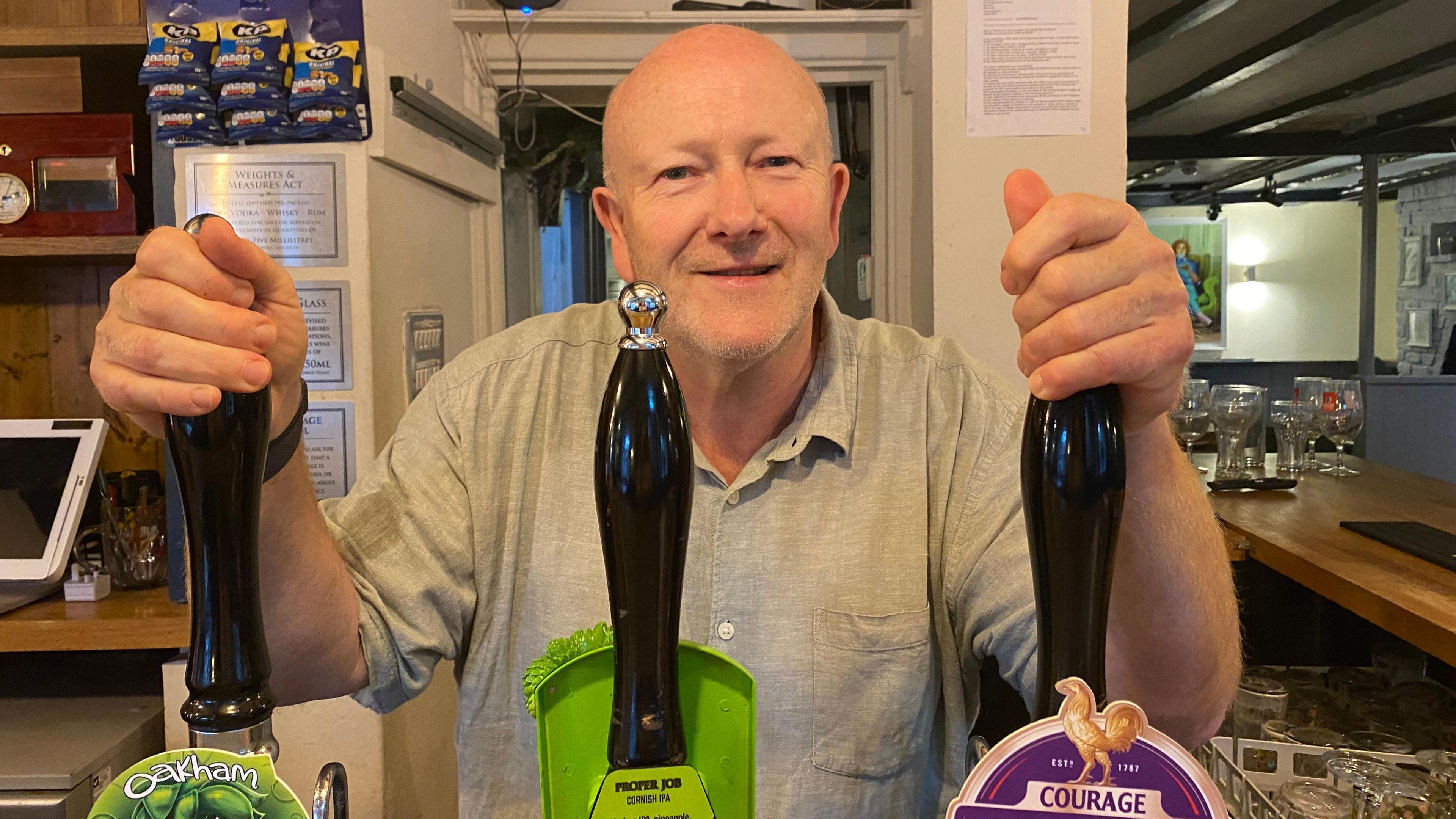 Keith Marsden wearing a grey t-shirt and holding the pumps of beer