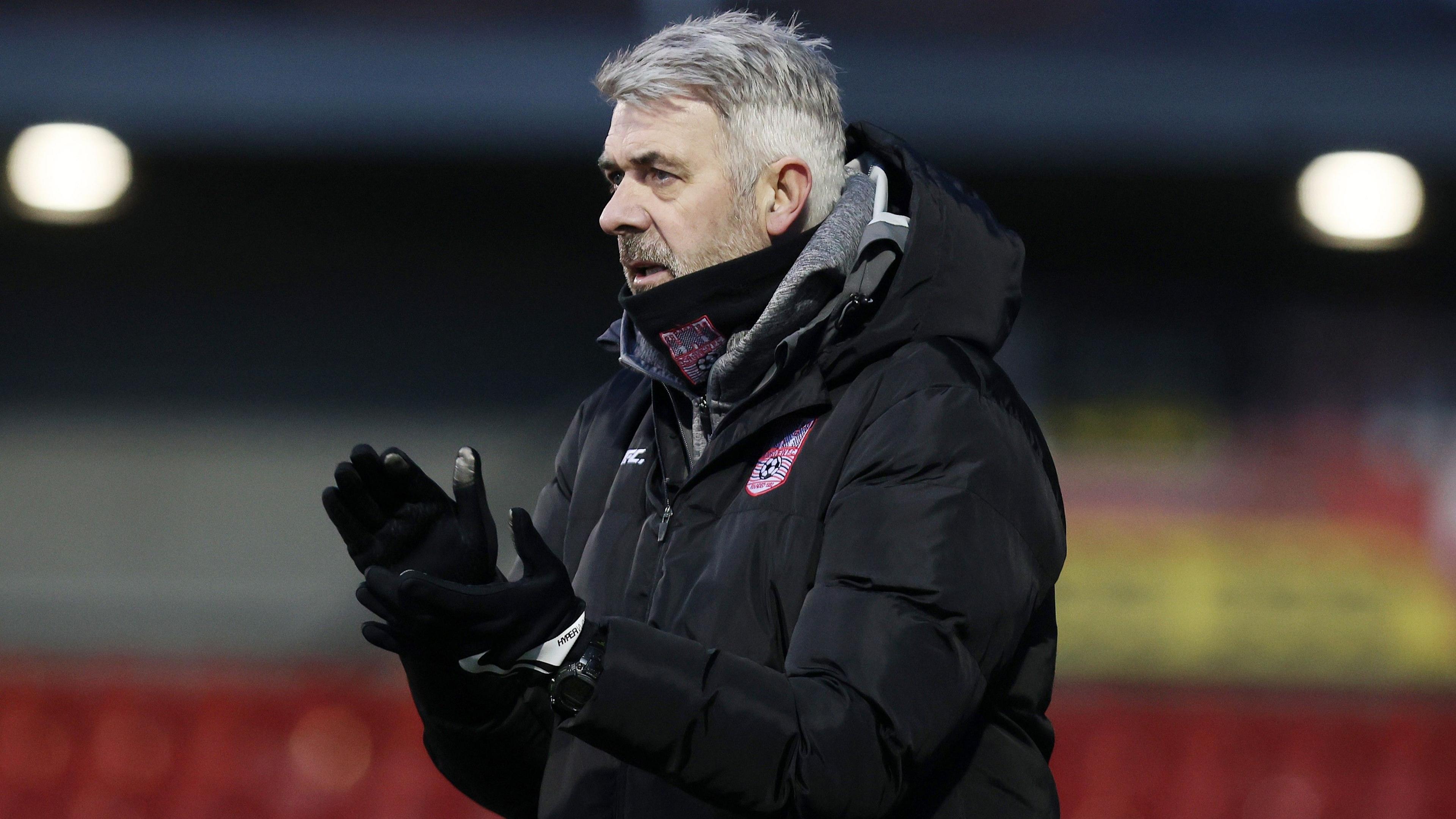 Tommy Canning, in a winter coat and wearing gloves, claps supporters