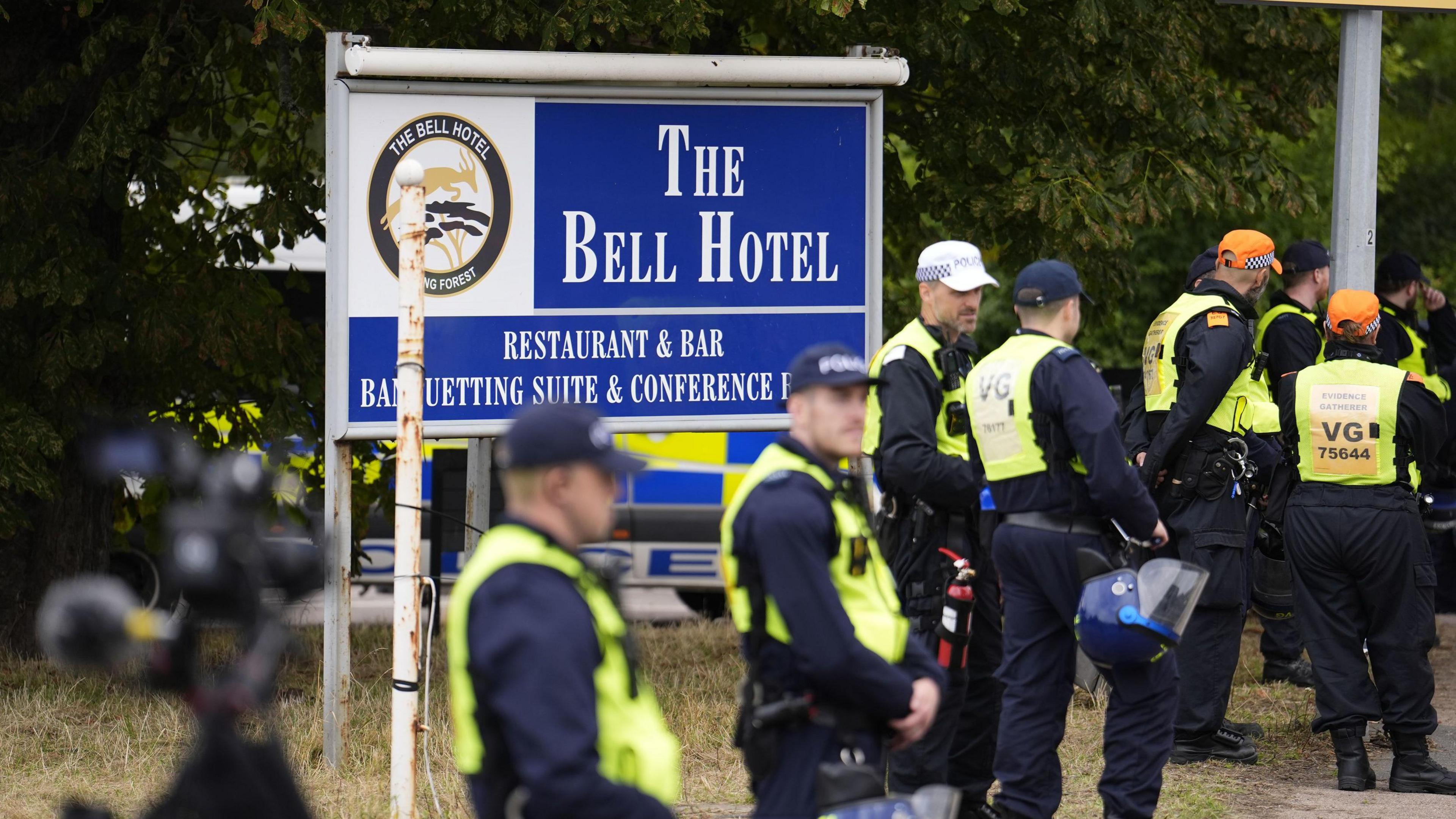 A group of police in high-vis vests stand outside a sign for The Bell Hotel in Epping.